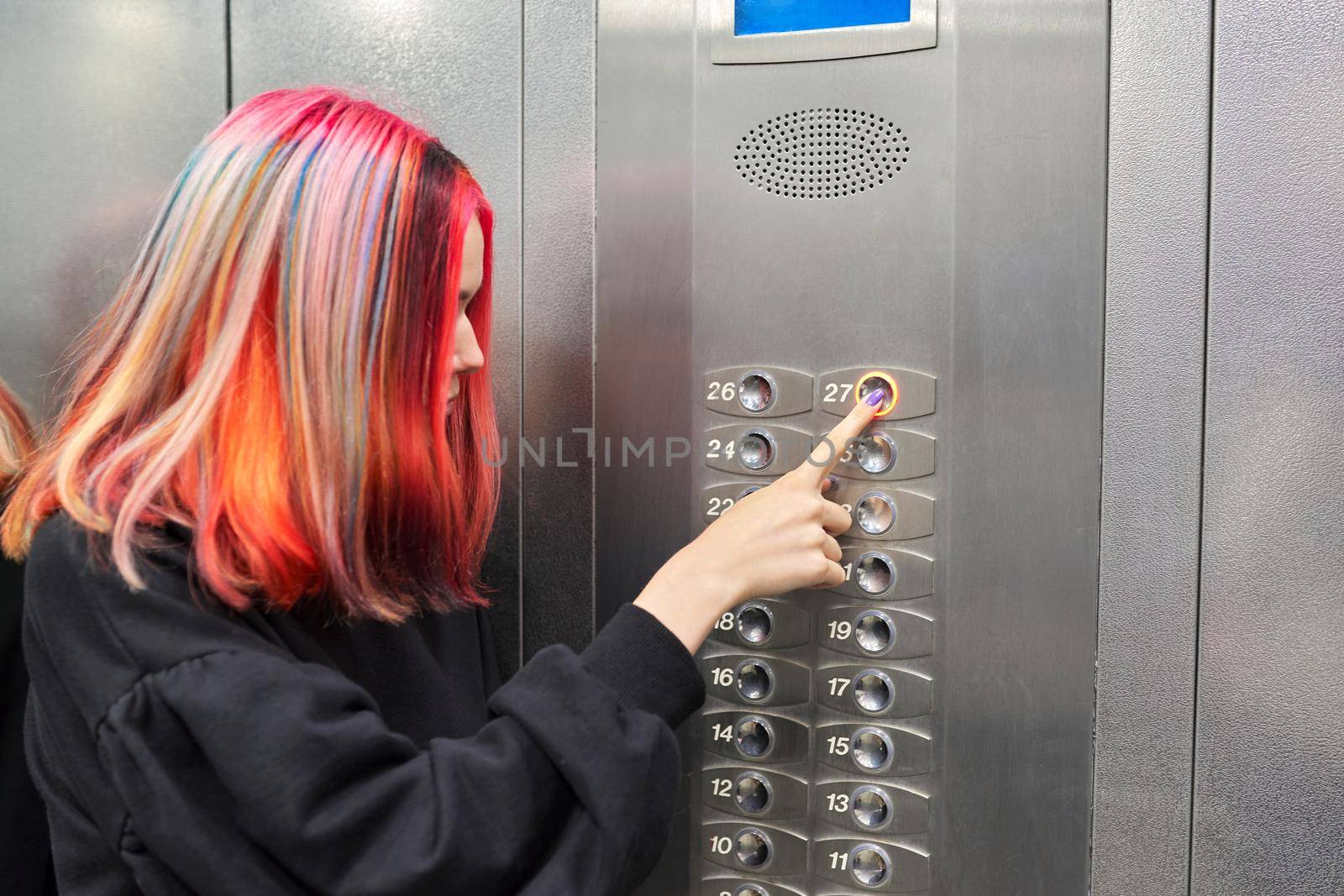 Female teenager pushing a button in the elevator. Woman pushing the top floor button in a skyscraper