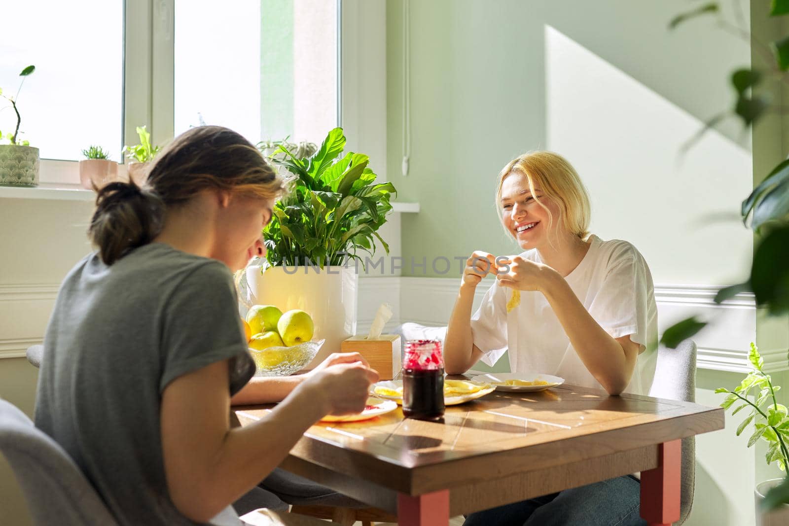 Teenagers guy and girl eating pancakes with jam, sitting at table at home. Homemade food, communication, teens, lifestyle concept