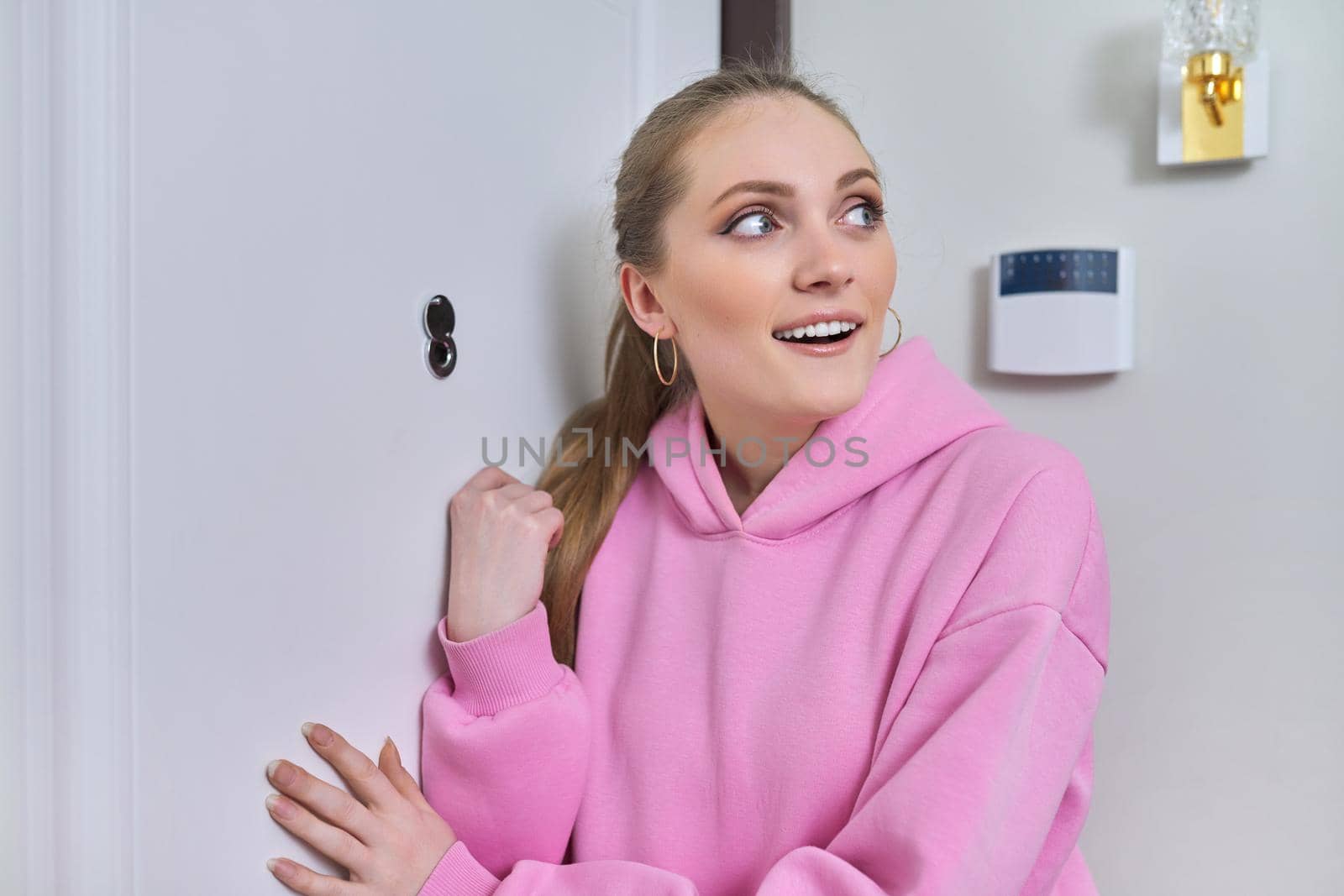 Young smiling woman standing near front door with peephole by VH-studio