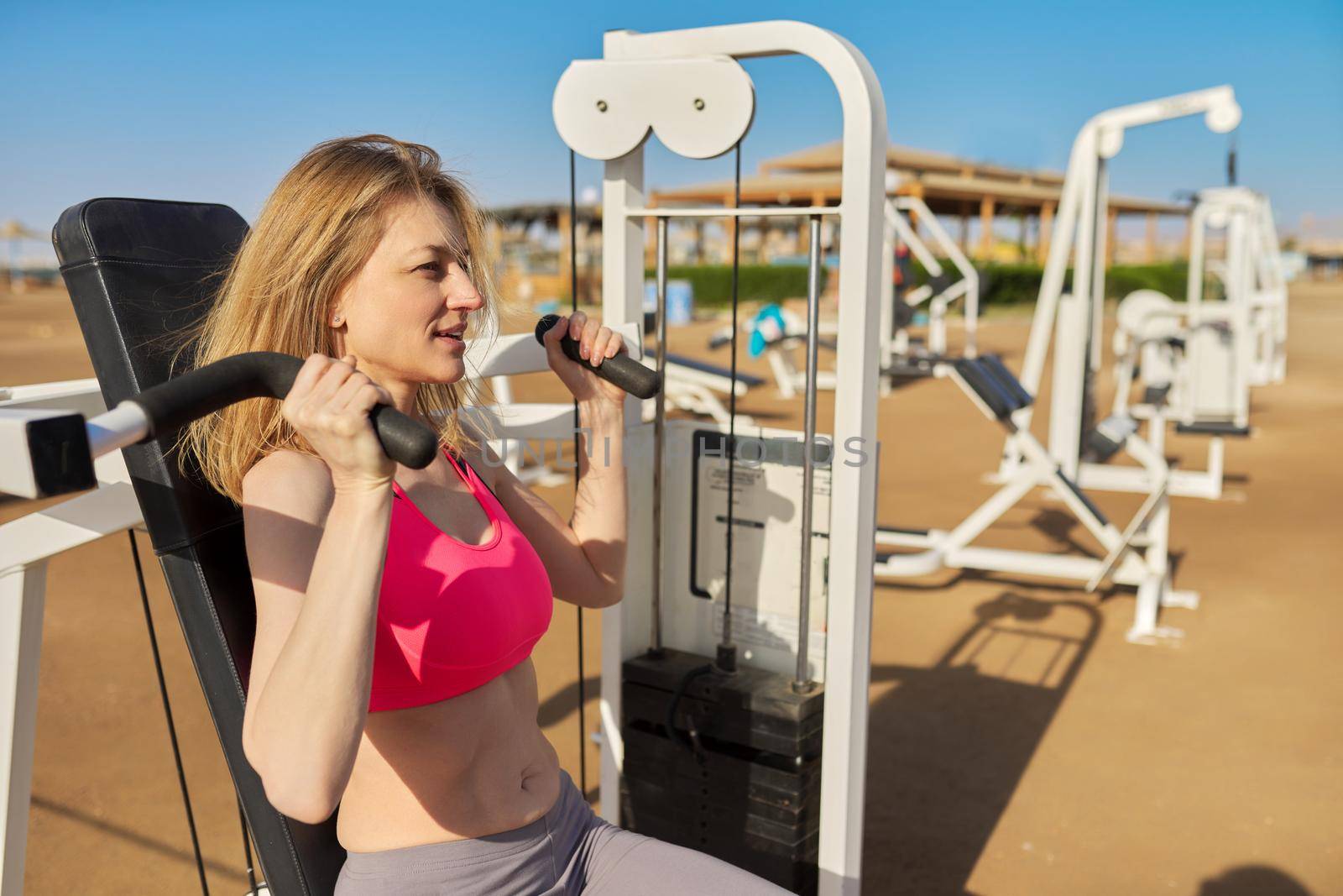 Middle aged woman in sportswear doing exercises on outdoor sports equipment by VH-studio