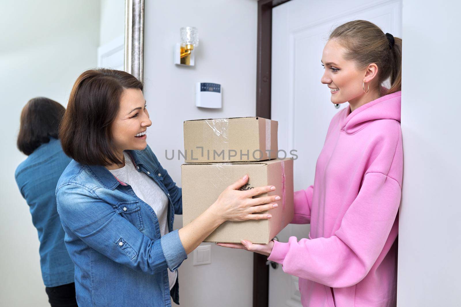 Online shopping delivery service, courier young woman with cardboard boxes near front door in apartment, adult woman buyer takes boxes