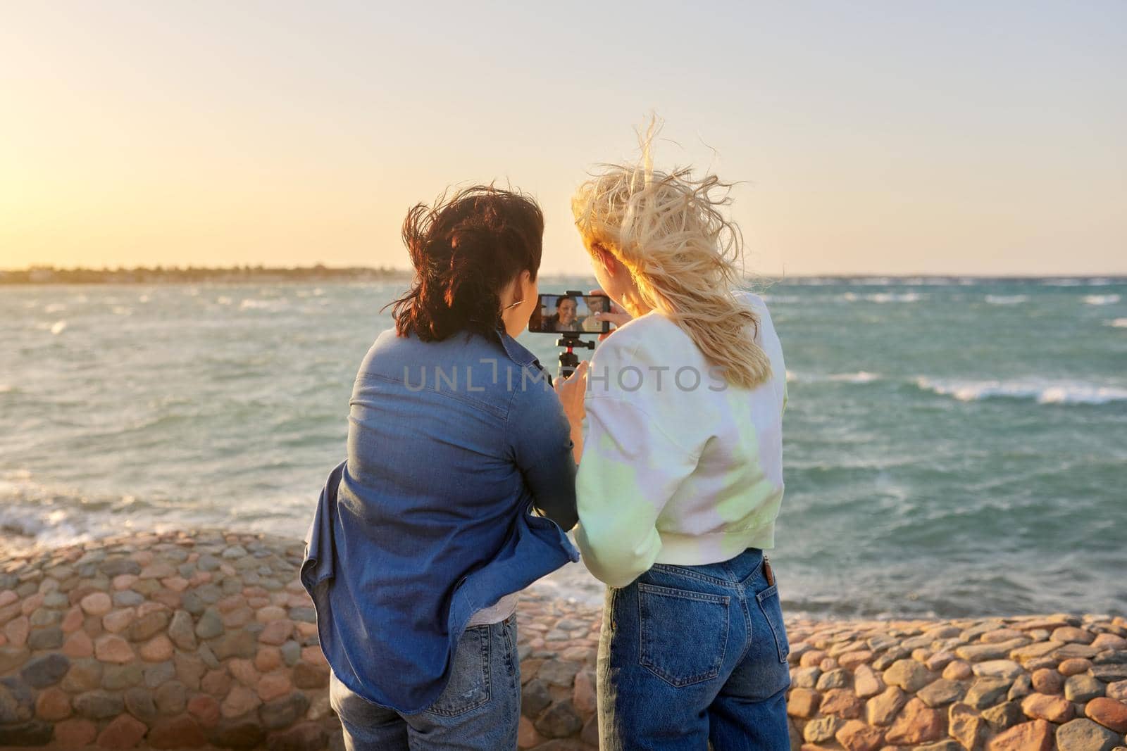 Sea vacation, females look at smartphone screen, make an online video call by VH-studio