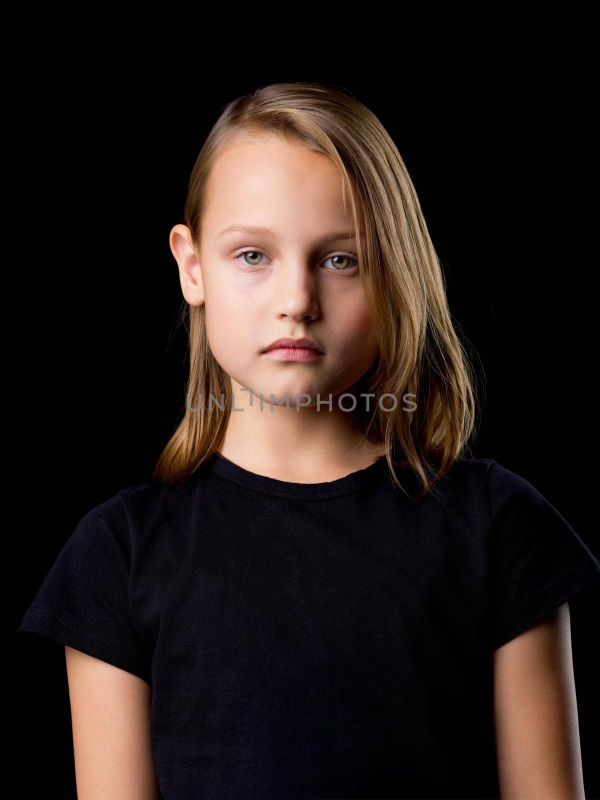 Beautiful girl posing in the studio. Close-up portrait of a beautiful blonde teenage girl in a black t-shirt on a black background.