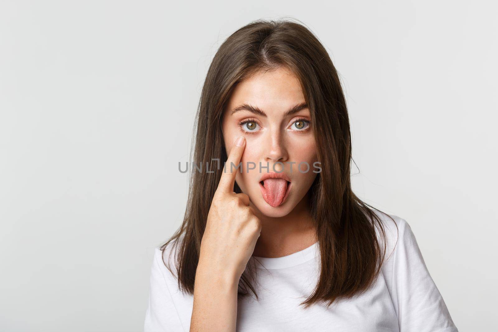 Close-up of silly attractive young girl showing tongue and pulling eyelid, watching you.