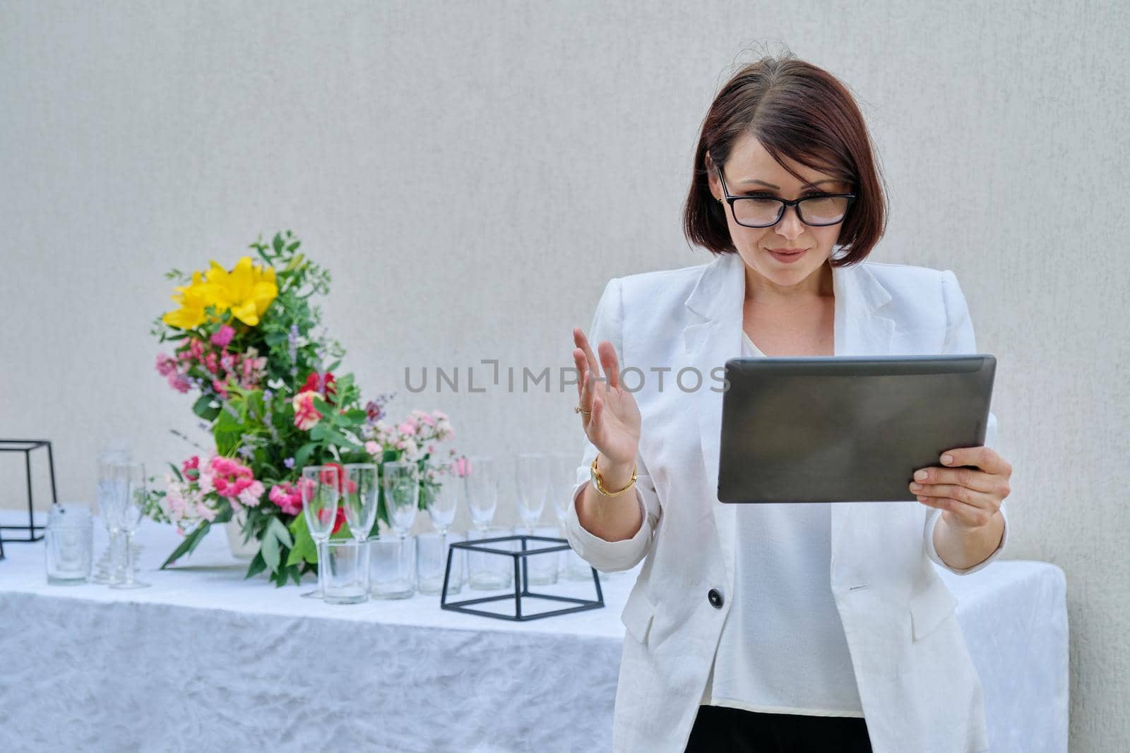 Organization of parties, ceremonies, professional woman event organizer with digital tablet, reserved holiday table decorated with flower arrangements. Female small business owner