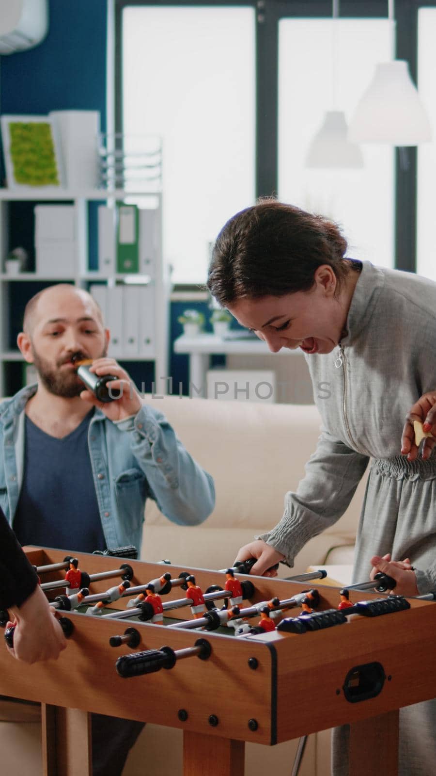 Multi ethnic coworkers playing foosball game at table for entertainment after work. Team of colleagues enjoying football play and having fun with leisure activity at office after hours