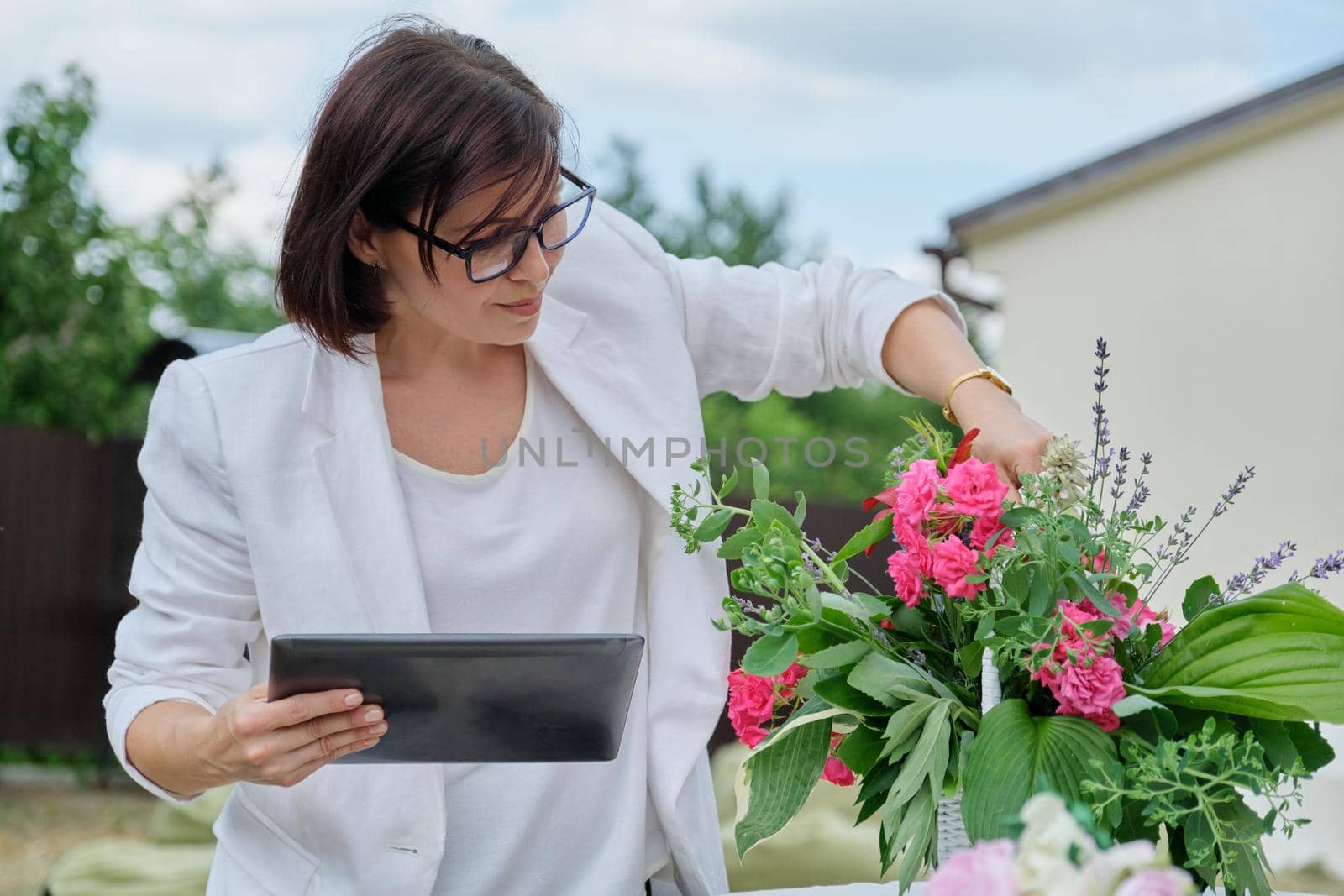 Organization of weddings, parties, event decoration. Business woman professional decorator florist with digital tablet working outdoors decorating ceremony. Female with flower arrangement