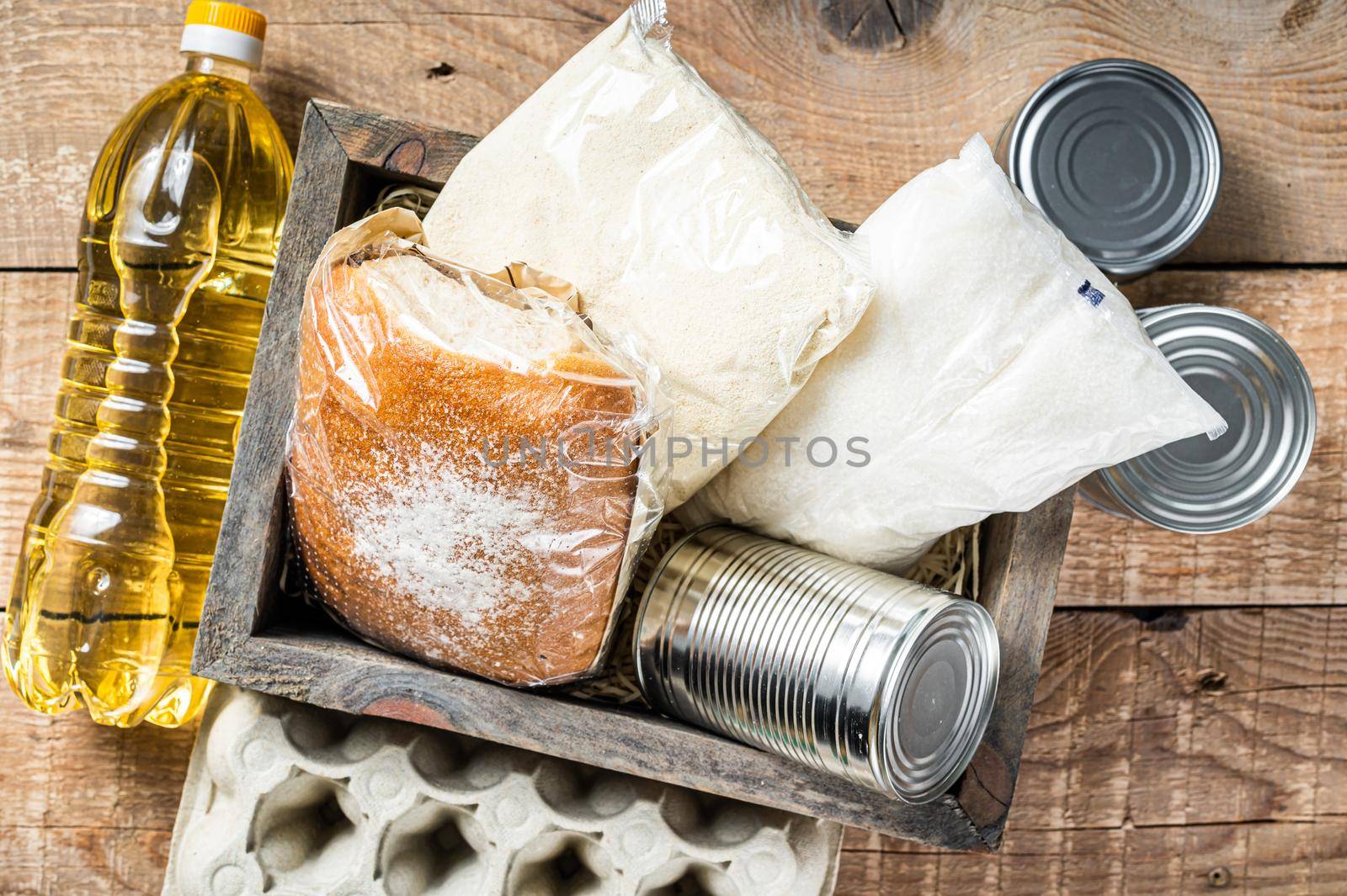 Wooden box with Donation food, quarantine help concept. Oil, canned food, pasta, bread, sugar, egg. Wooden background. Top view by Composter