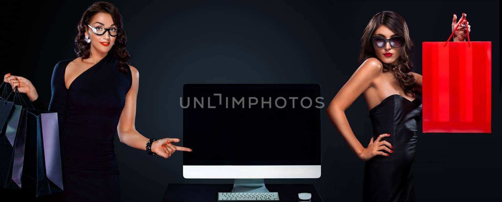 Black friday and Cyber Monday sale concept for shop. Two women holding bags and pointing on computer isolated on dark background by MikeOrlov