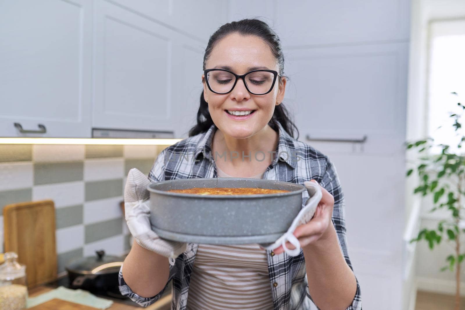 Portrait of smiling woman in kitchen mittens holding hot freshly baked apple pie by VH-studio