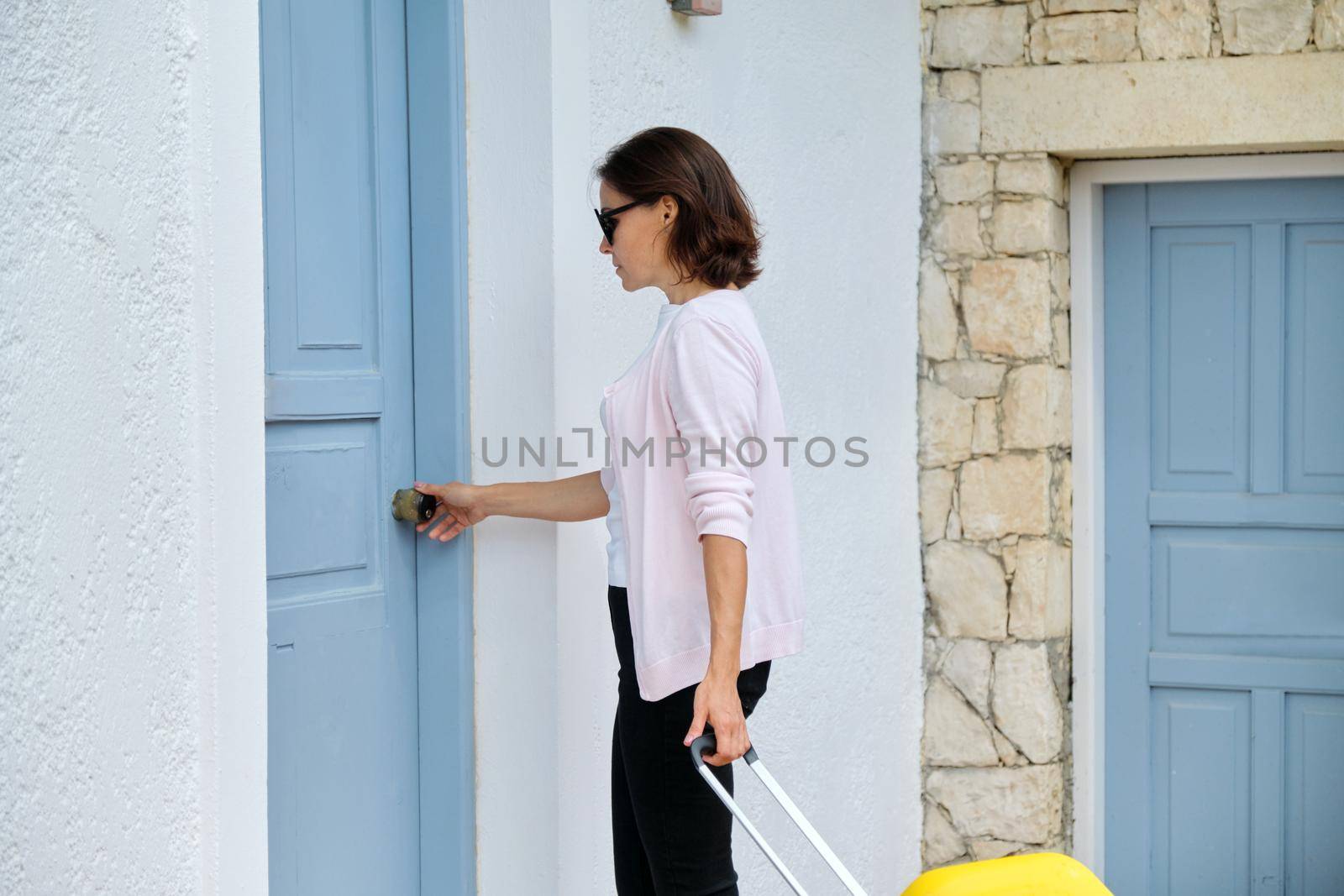 Tourism, travel, resort, vacation, rental of real estate, accommodation in a villa. Outdoor, woman traveler with yellow suitcase opening closing door of the house