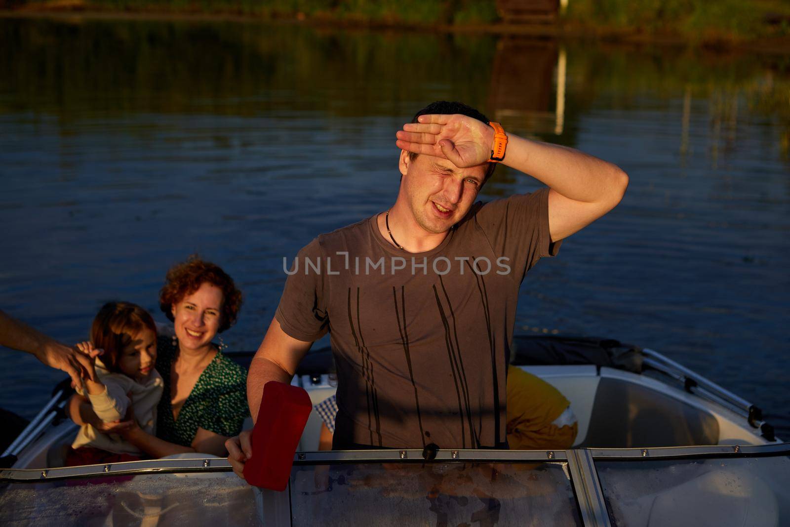 Adult male protecting face from sunlight while riding motorboat with family on summer day on lake
