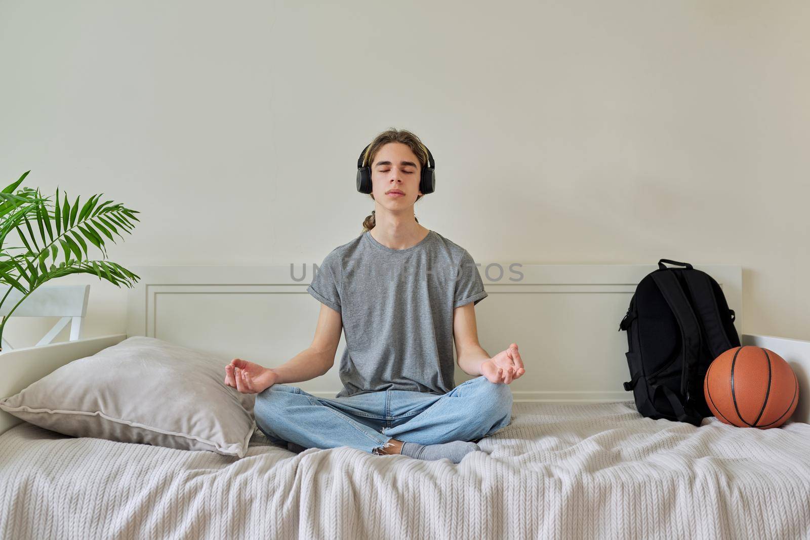 Male teenager sitting in lotus position on bed relaxing meditating by VH-studio
