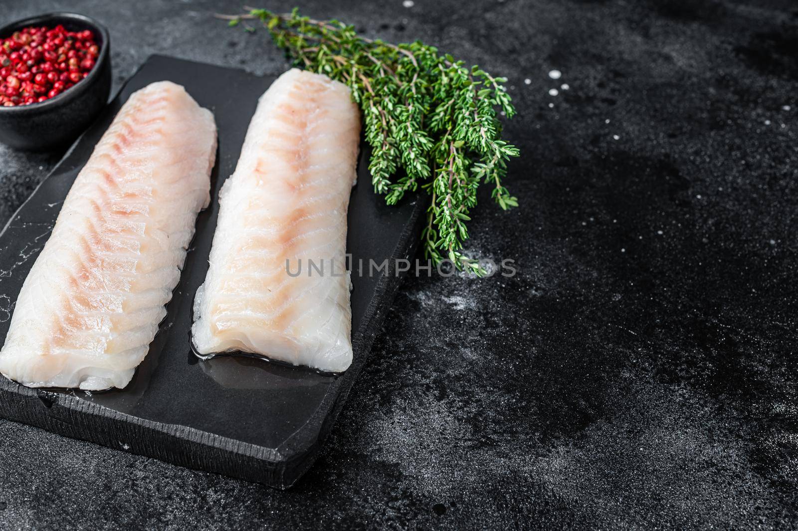 Raw cod loin fillet fish on marble board. Black background. Top view. Copy space.