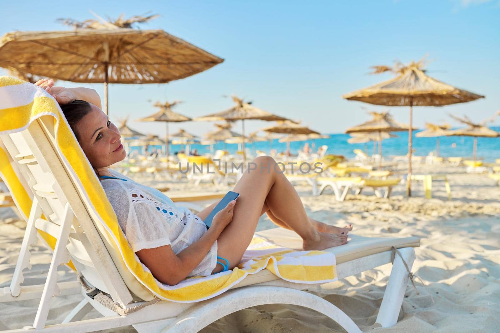 Relaxing mature woman sitting on sun lounger on the beach. Vacation, weekend by the sea, relaxation, middle-aged summer people, copy space