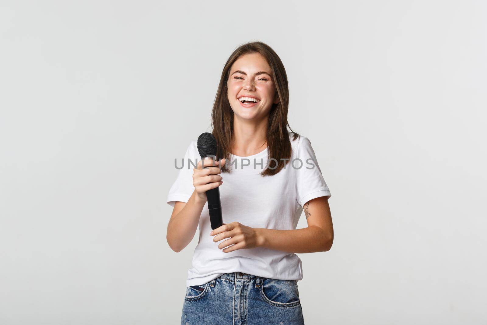 Happy laughing girl holding microphone and singing karaoke, white background.