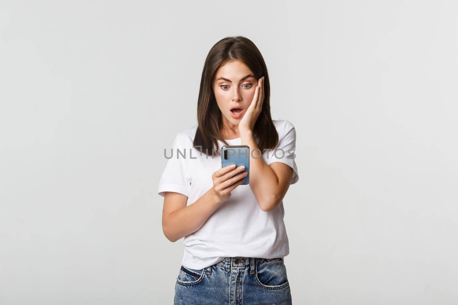 Shocked and impressed brunette girl looking amazed at smartphone screen.