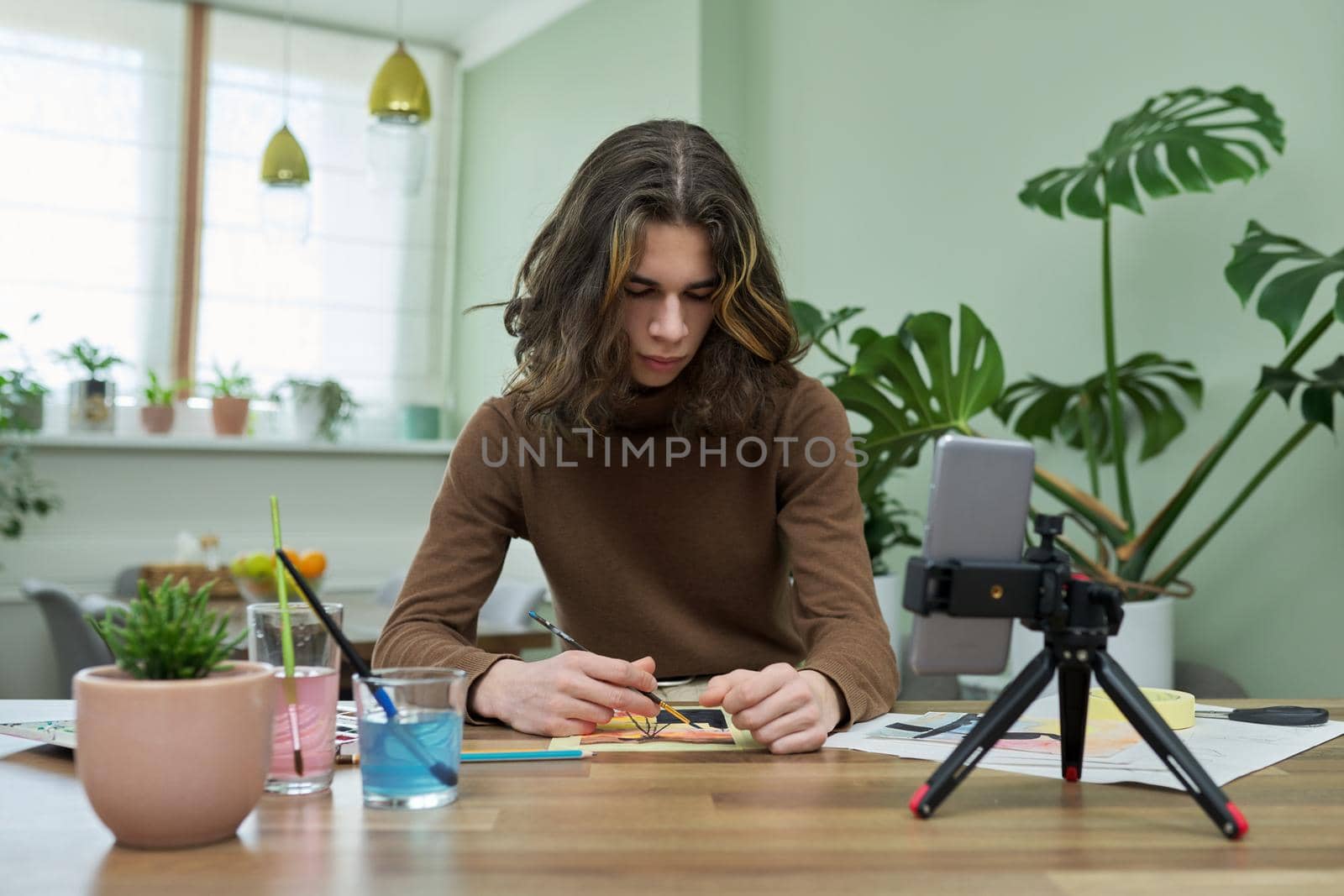 Teenage guy drawing with watercolors, watching video class on smartphone by VH-studio