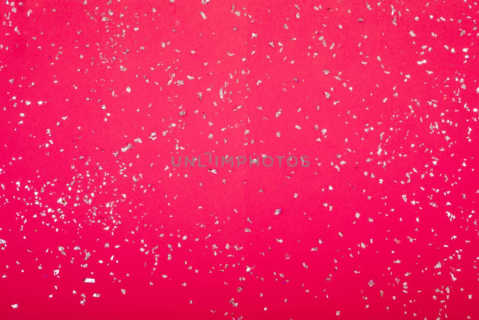Silver sparkles scattered randomly on juicy pink background. Silver confetti on a pinkbackground. Holidays banner with place for text