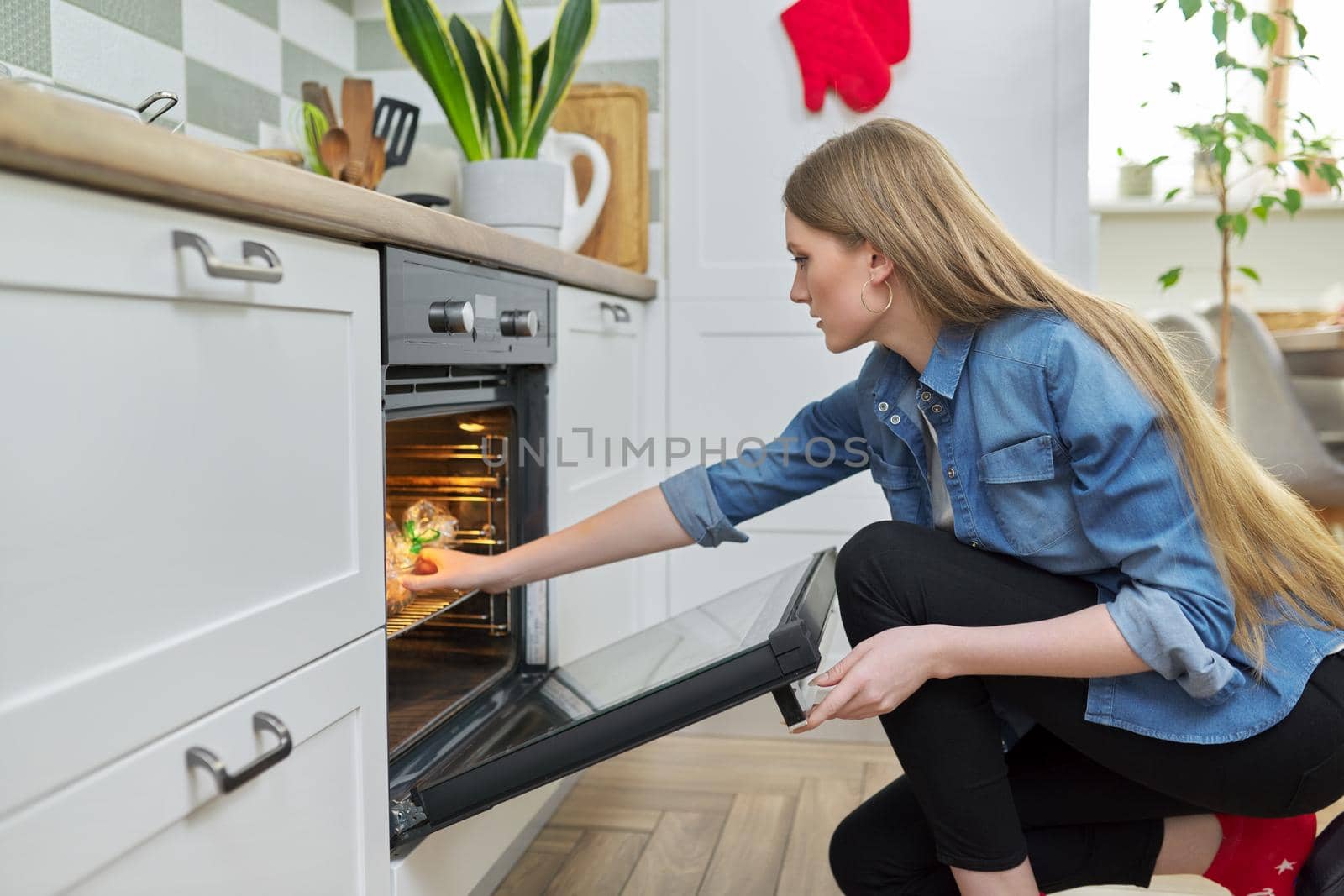 Young woman putting marinated chicken in baking bag in oven by VH-studio