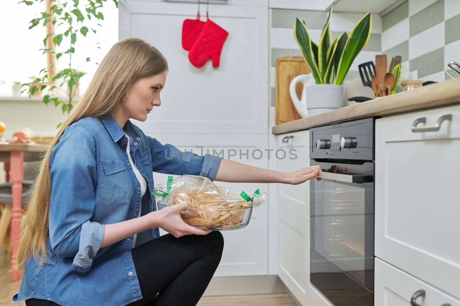 Young woman putting marinated chicken in baking bag in oven by VH-studio