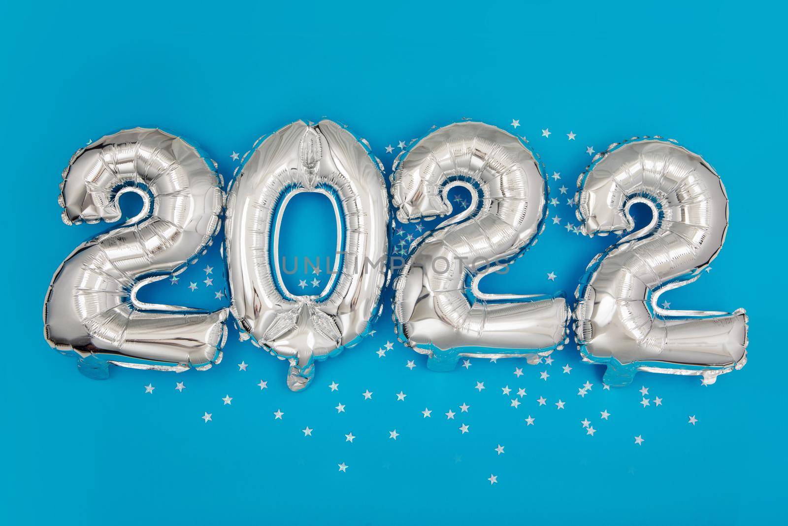 From above of silver number balloons showing 2022 year on blue background with star shaped confetti