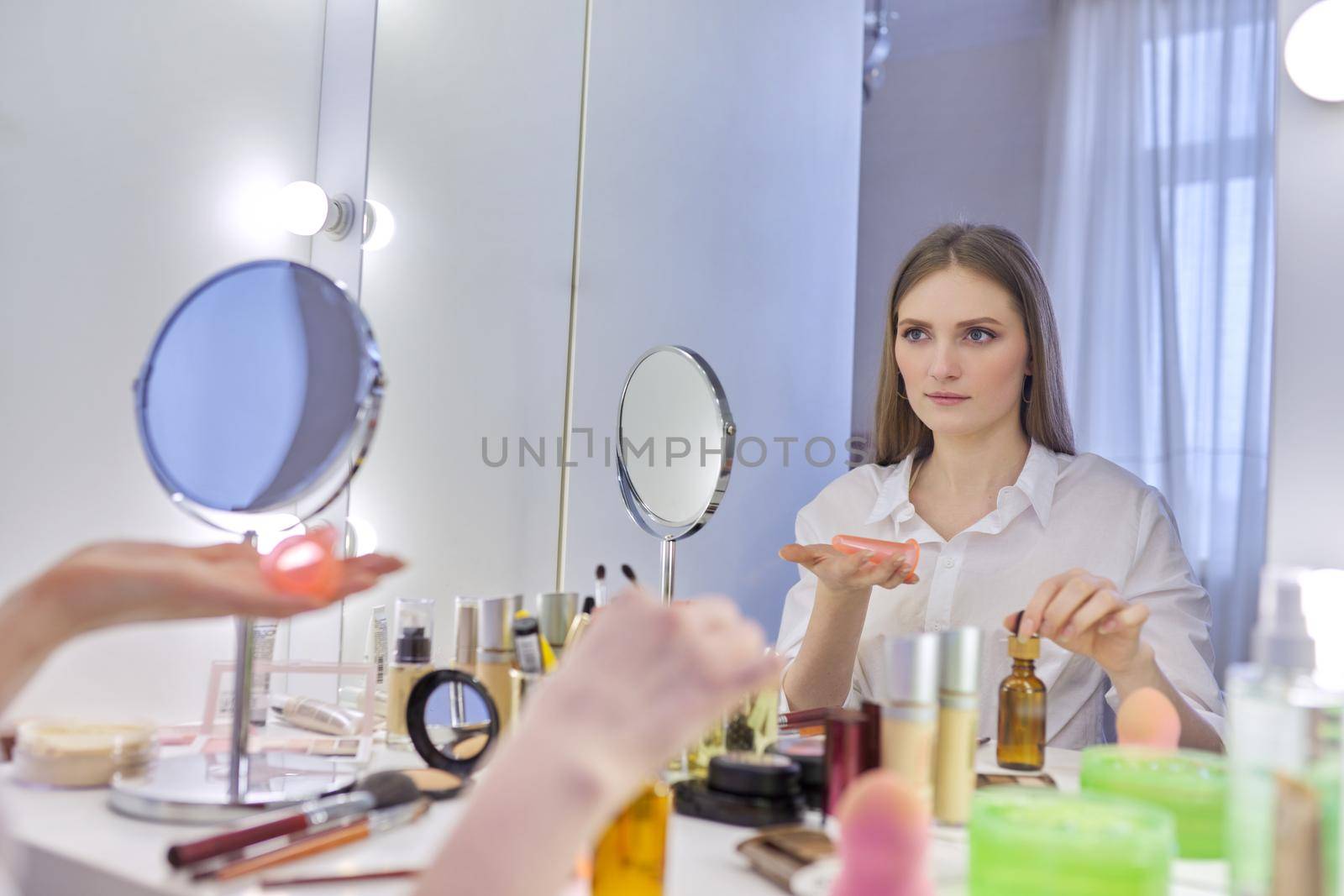 Young beautiful woman doing facial massage with silicone tools cosmetic vacuum jars, using massage oil. Female sitting at home at make-up table with mirror, caring for skin of face, home spa treatment