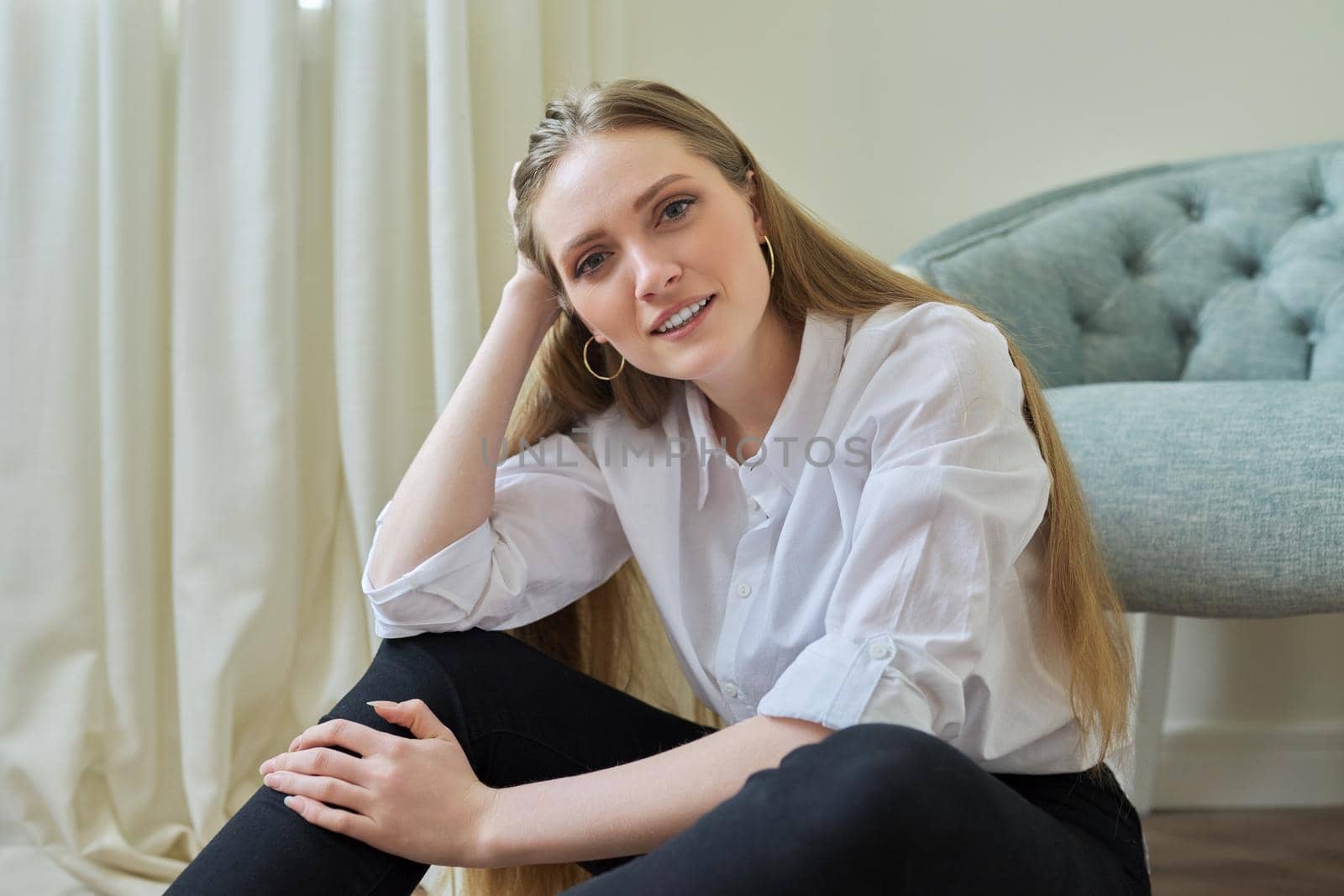 Portrait of beautiful smiling confident blonde looking at camera, female sitting at home on floor