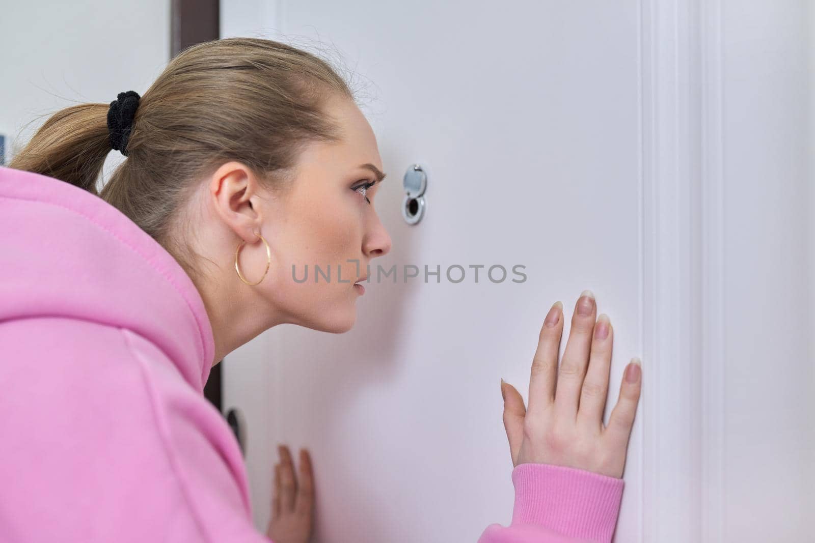 Young woman looking through peephole of front door in apartment. by VH-studio