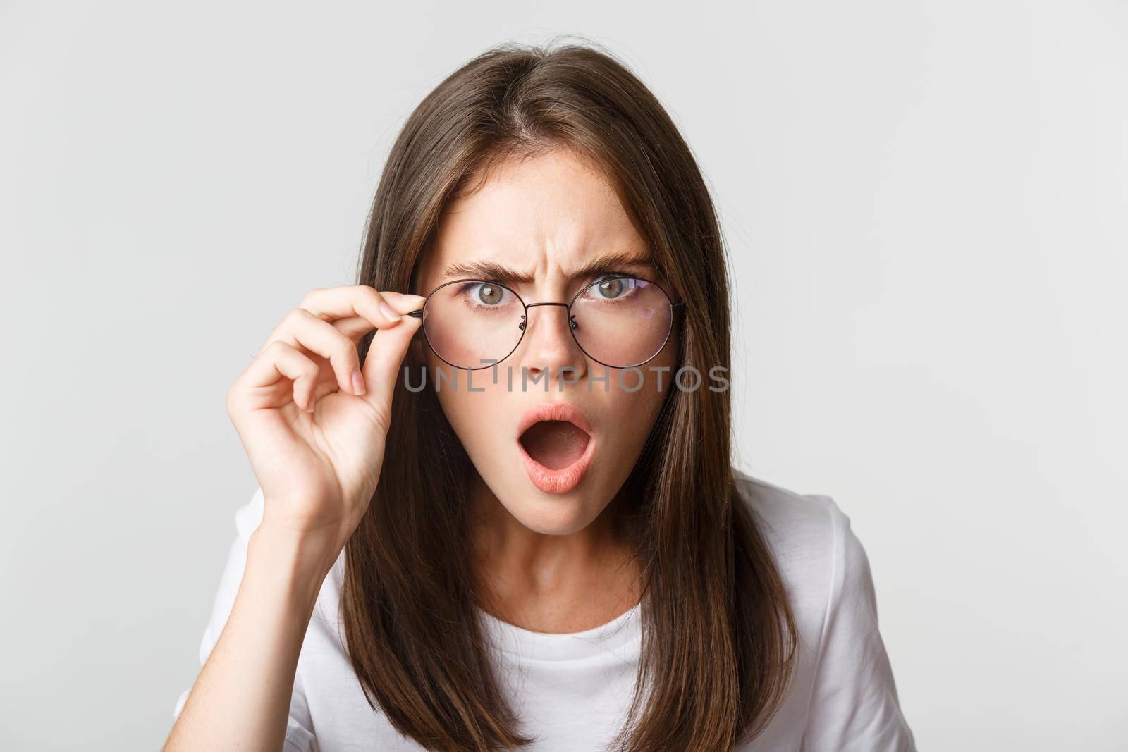 Close-up of insulted and shocked young angry woman looking from under glasses by Benzoix