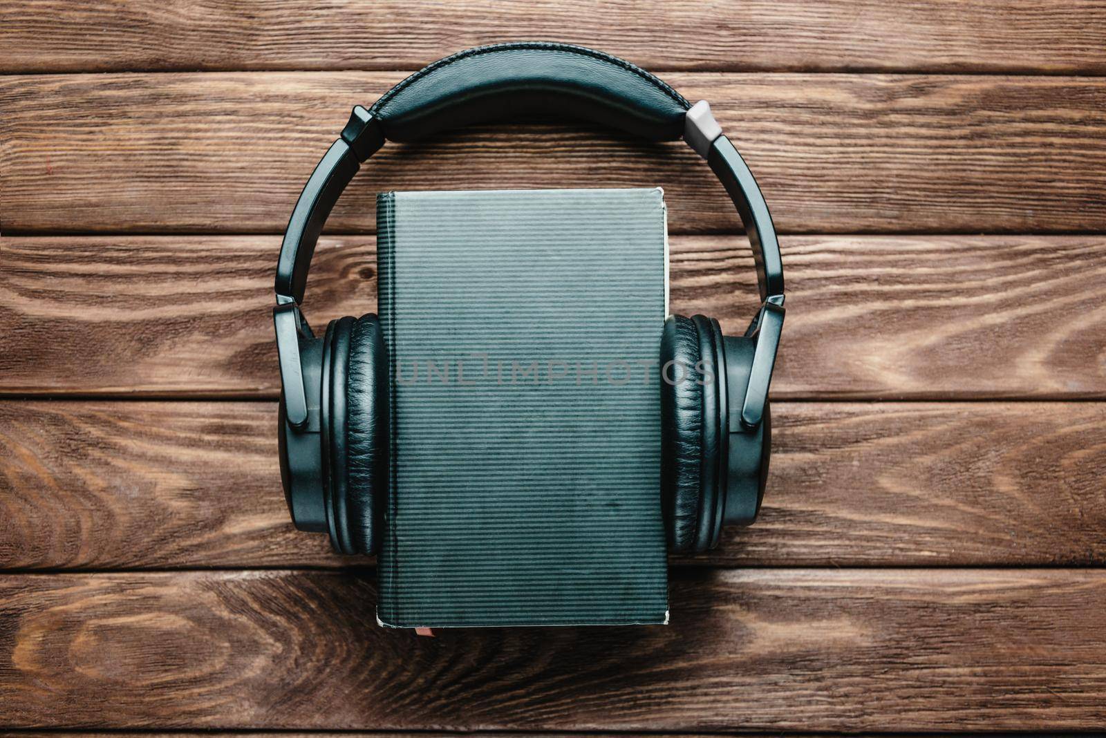 Headphones around a paper book on a wooden background, space for text on the cover of book. Concept of audiobook.
