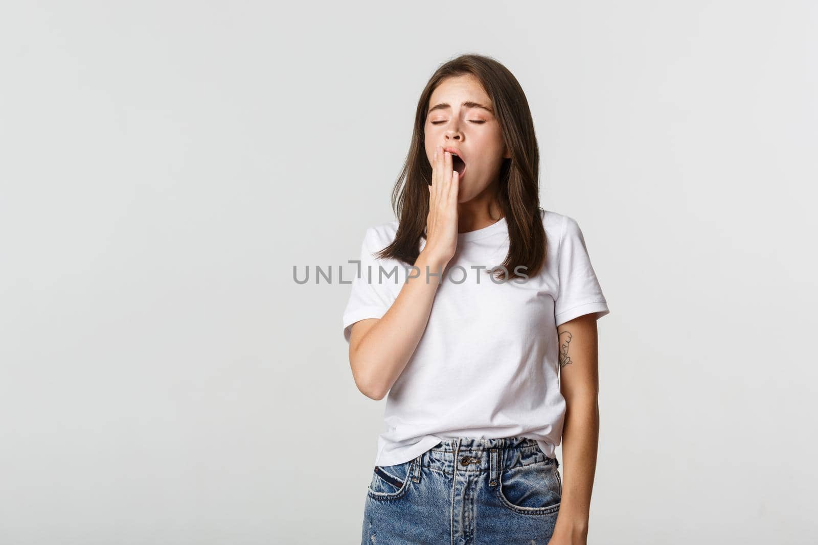 Portrait of attractive young female student yawning tired, feeling sleepy, white background.