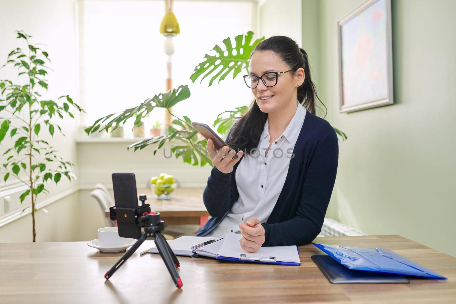 Business woman working remotely using video call. Female freelancer, teacher, psychologist, financial legal specialist sitting at home looking at smartphone webcam, talking, consulting teaching online