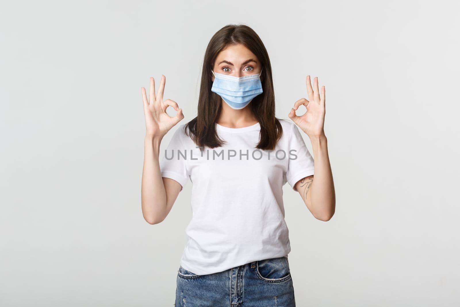 Covid-19, health and social distancing concept. Excited smiling pretty girl in medical mask showing okay gesture satisfied.