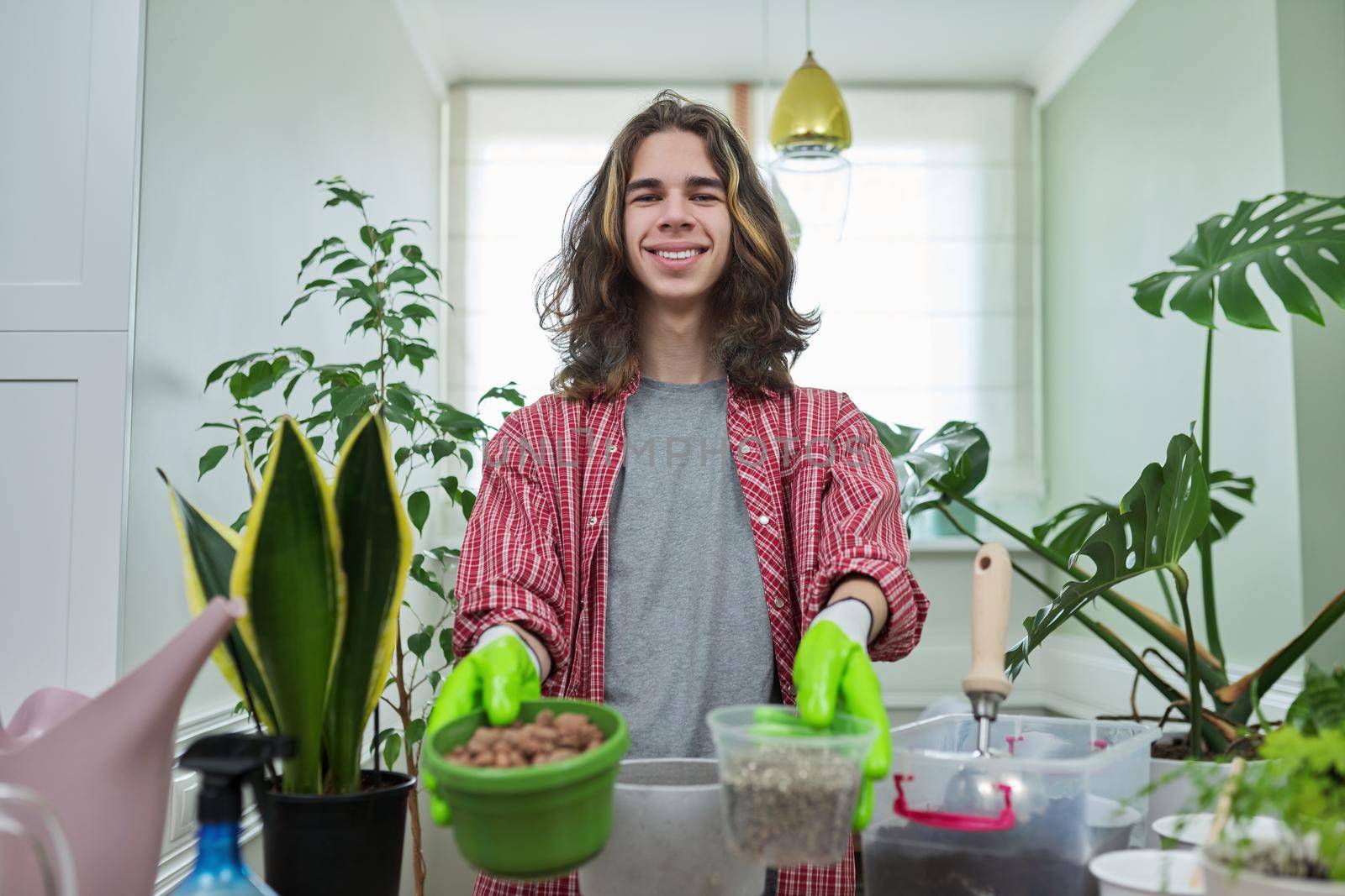 Green eco hobby of young male, teenager showing plant, soil, expanded clay, soil additives perlite vermiculite at camera, recording video for plant vlog blog. Eco green trends, modern city apartments