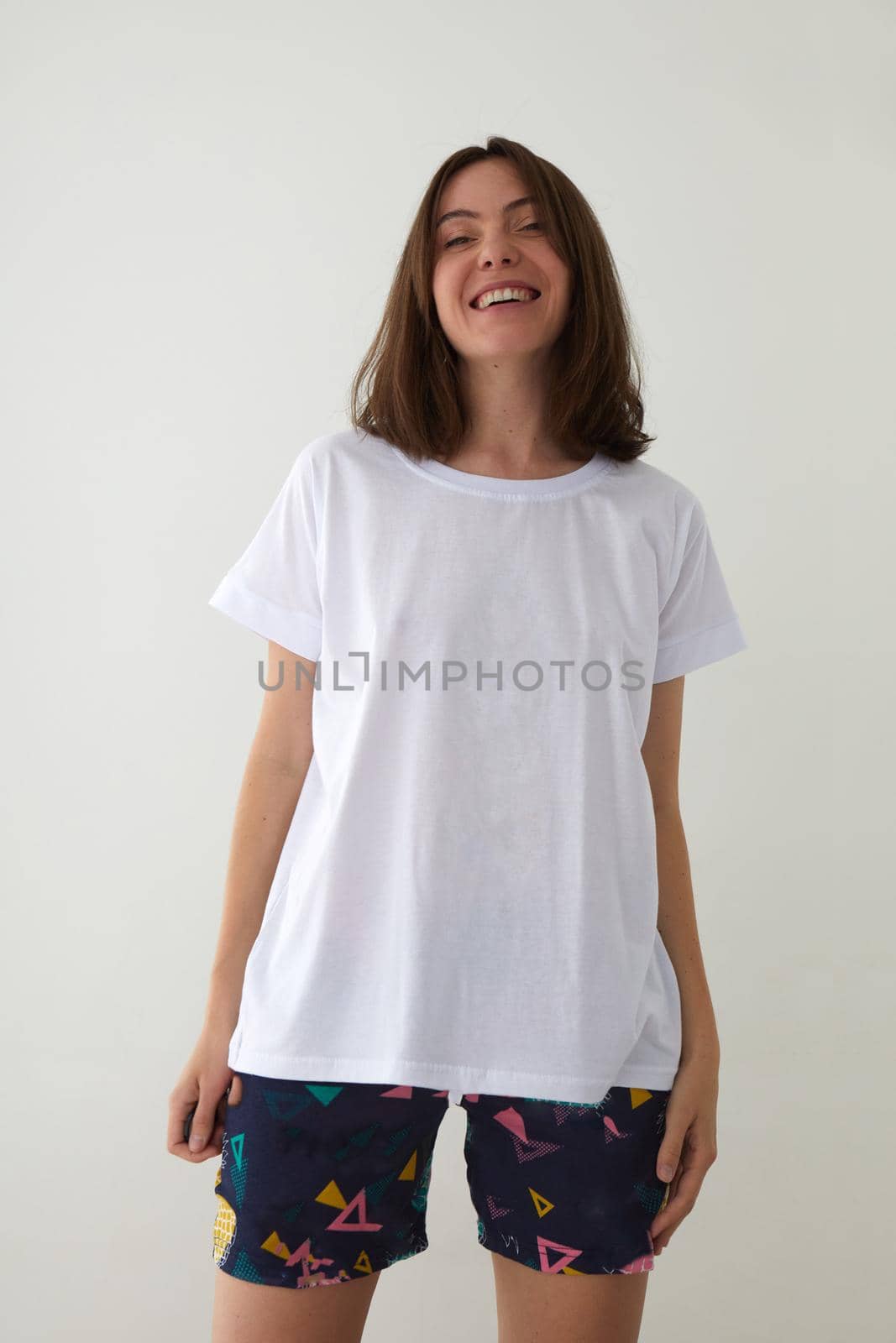 Delighted young female in white t shirt and shorts standing on white background in studio and looking at camera