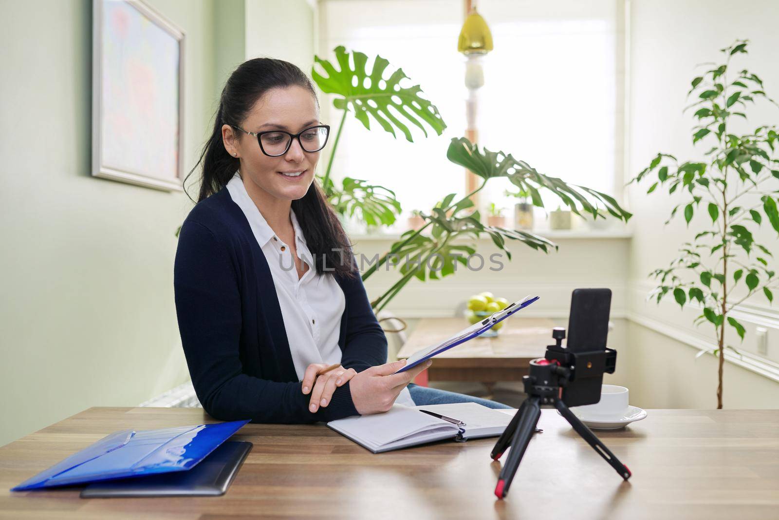 Business woman looking in smartphone webcam on tripod at home. Female talking online recording video blog, consulting finance, mentoring teaching training remotely, helping psychologist, distance work