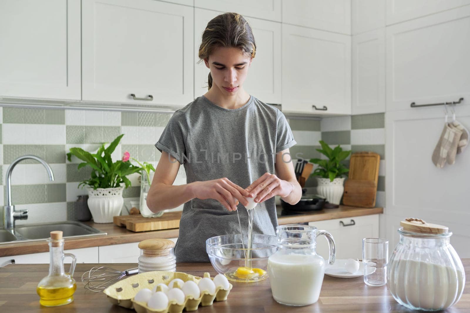 Guy teenager cooking pancakes at home in the kitchen, cooking hobby of young male