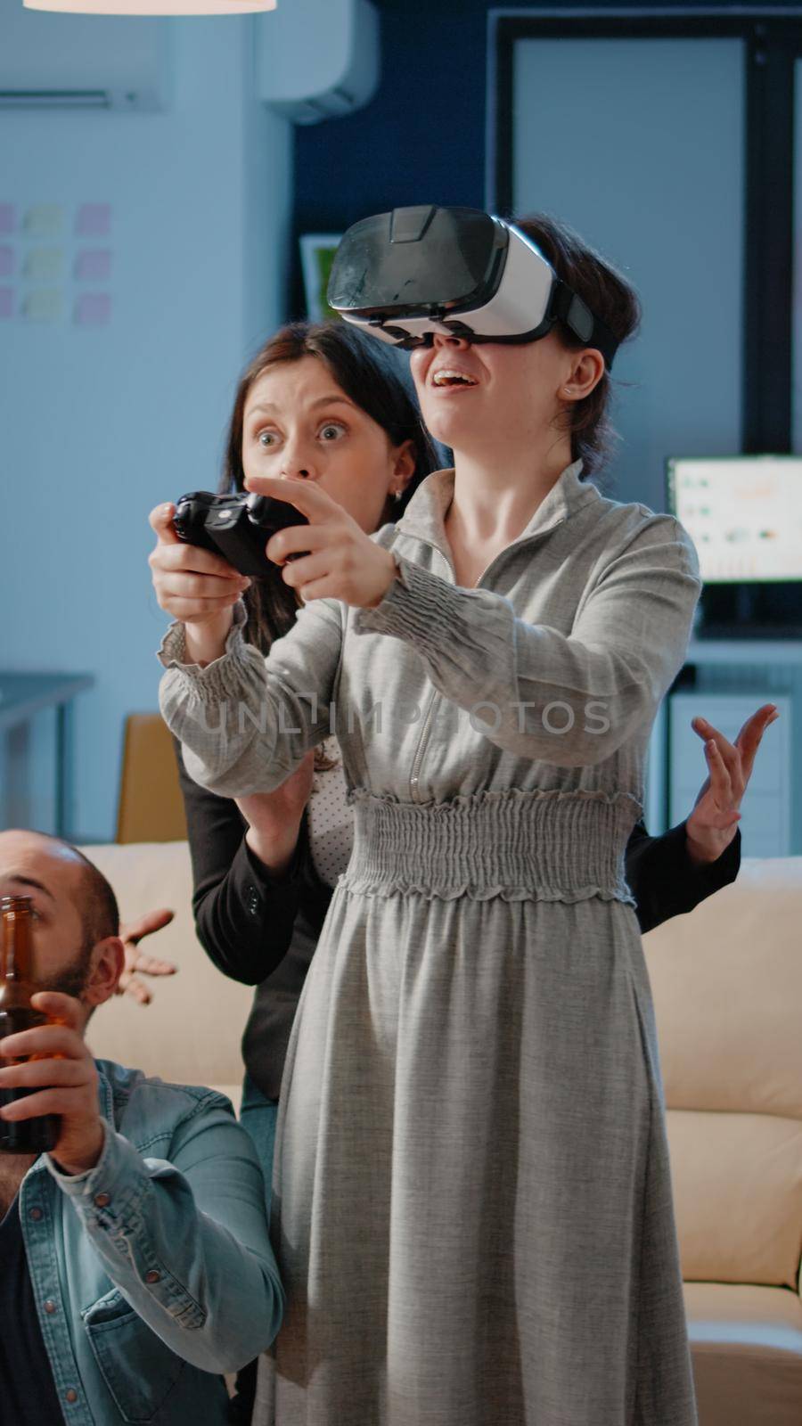 Woman using joystick and vr glasses while workmates cheering after work. Coworkers enjoying video games to play game on tv console with virtual reality goggles and controller at office