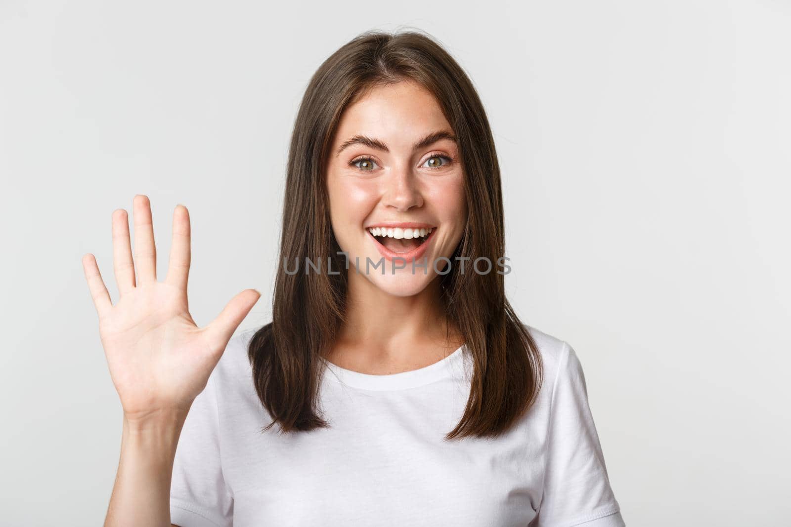 Close-up of cheerful attractive young woman smiling, showing five fingers, white background.