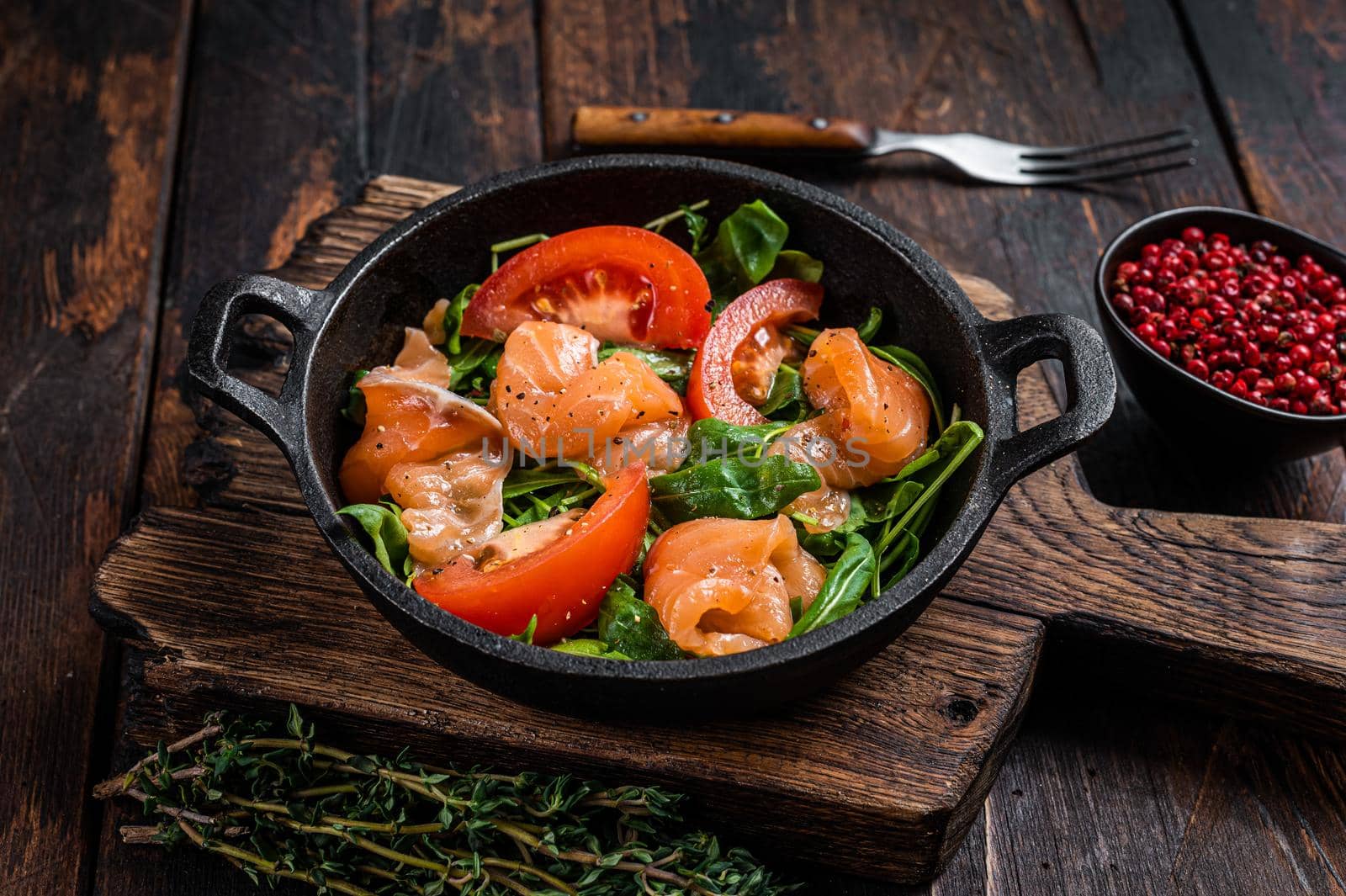 Fresh salmon salad with arugula, tomato and green vegetables. Dark wooden background. Top View.