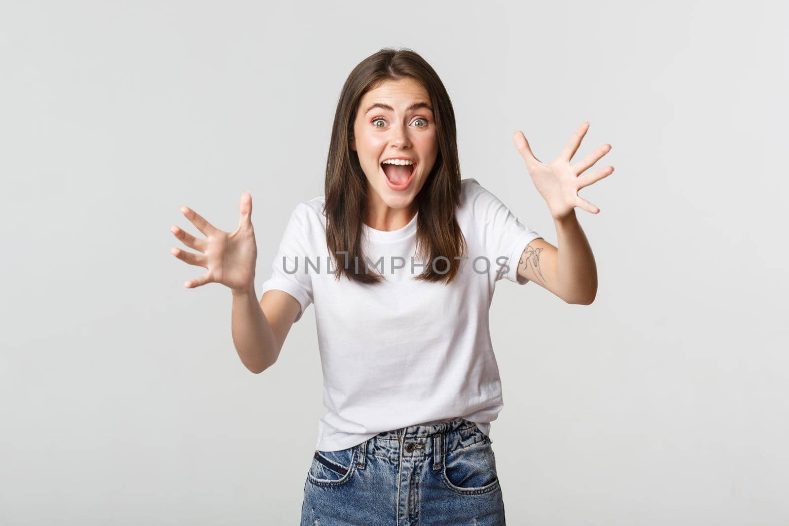 Excited brunette girl smiling amazed and raising hands to catch something by Benzoix