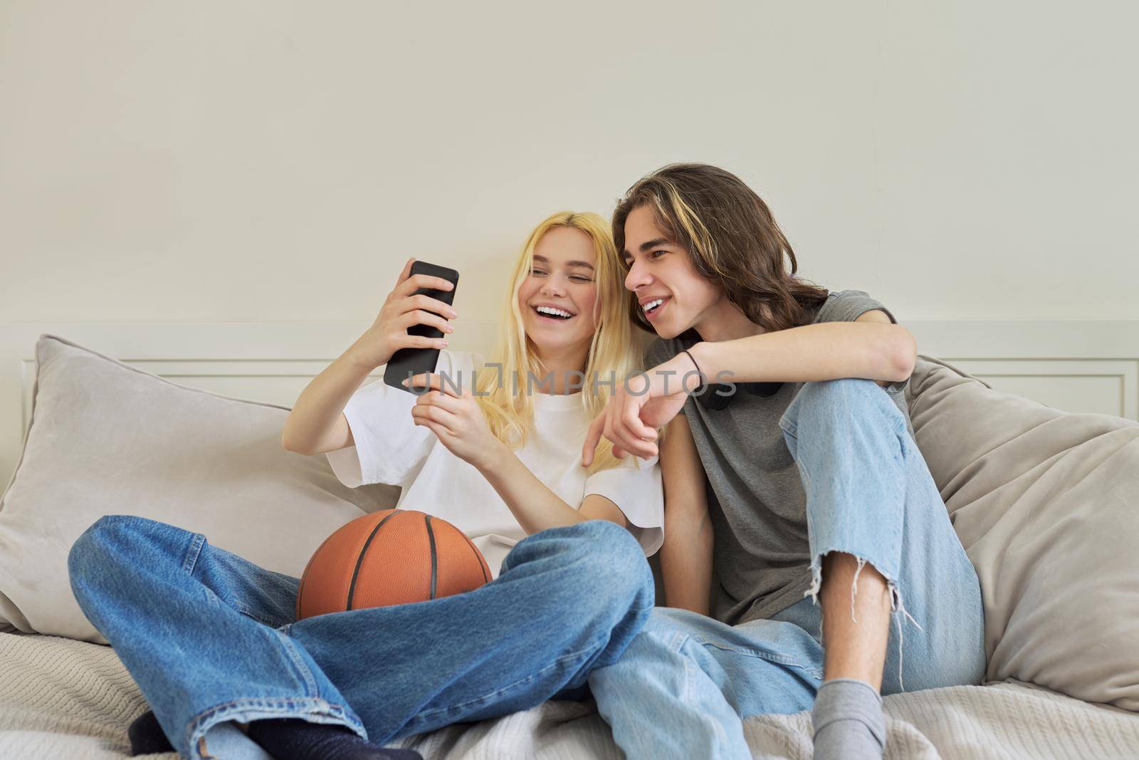 Happy laughing hipster teenagers male and female having fun using smartphone together. Couple takes photos chat online using video call. Lifestyle, technology, friendship, communication of adolescents