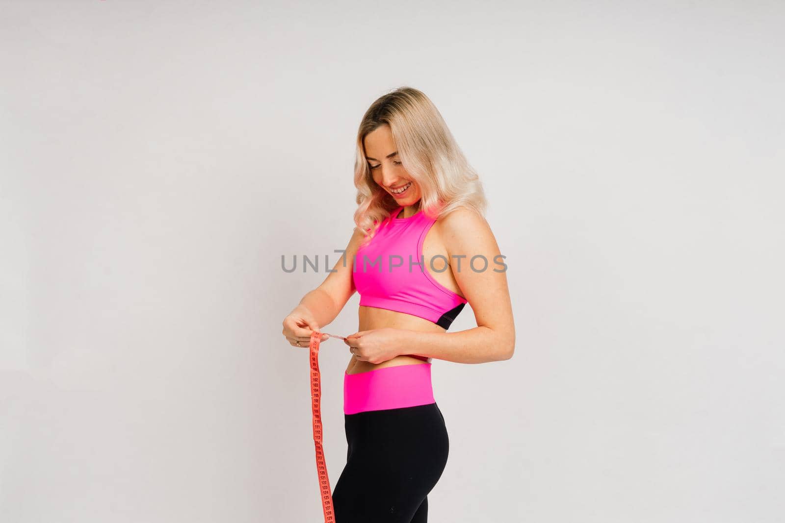 Fitness woman with tape measure showing her waist on studio background by Zelenin
