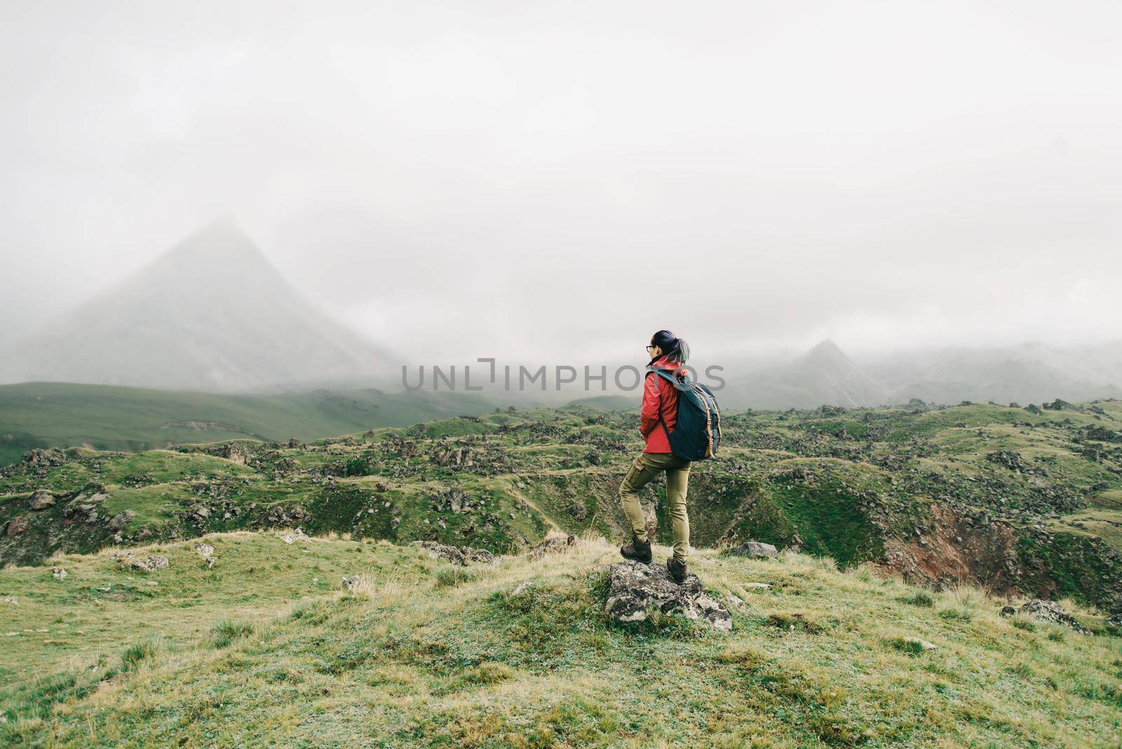 Hiker young woman with backpack walking in mountain valley. In the background a mountain in fog.