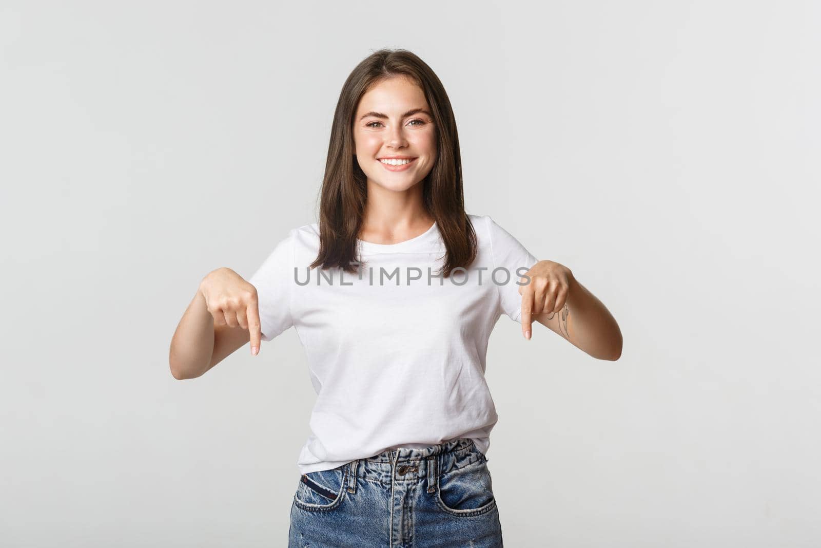 Satisfied smiling brunette girl pointing fingers down, recommend product.