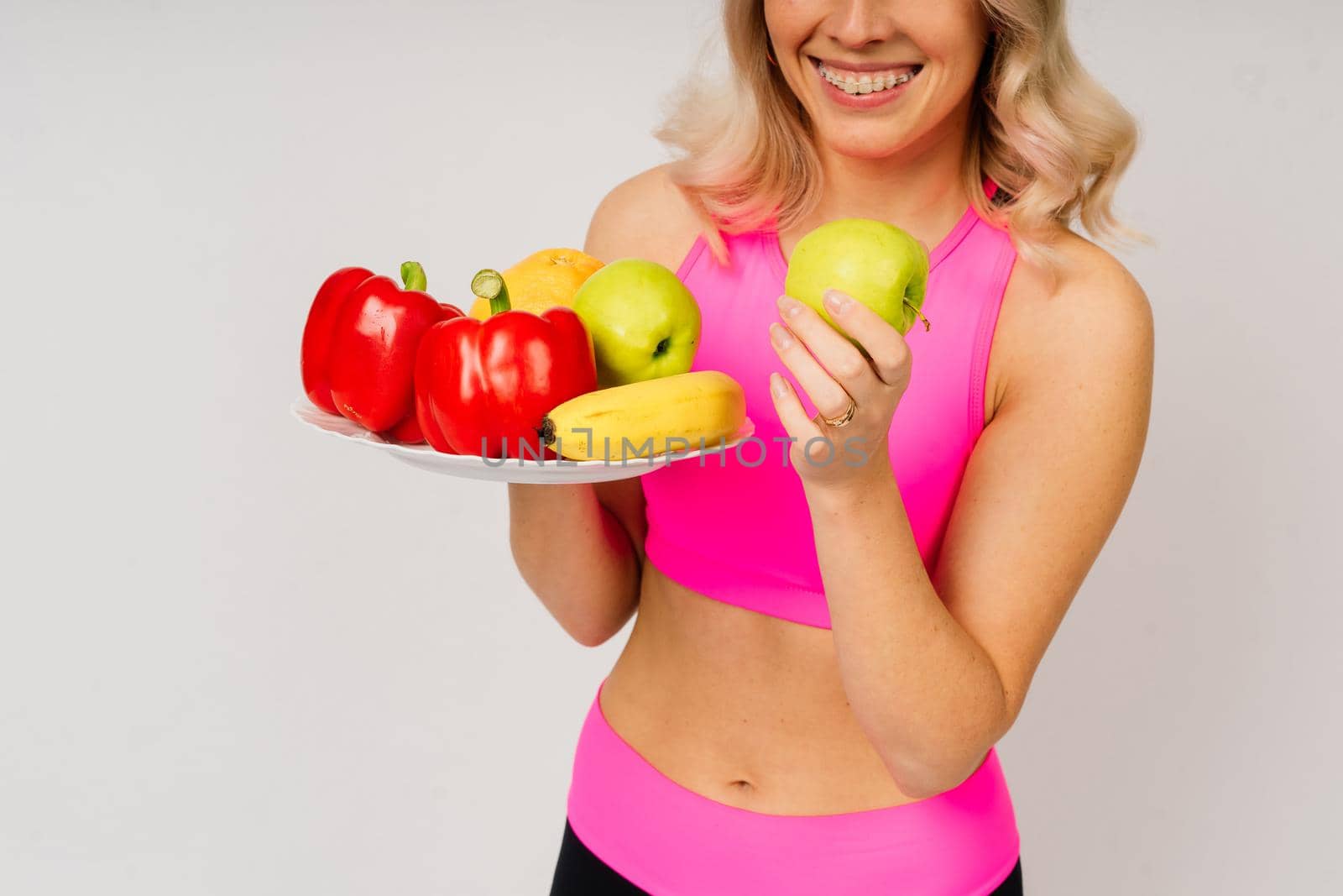 Studio shot of young fitness woman in a sports clothing holding green apple, fruits, vegetables.