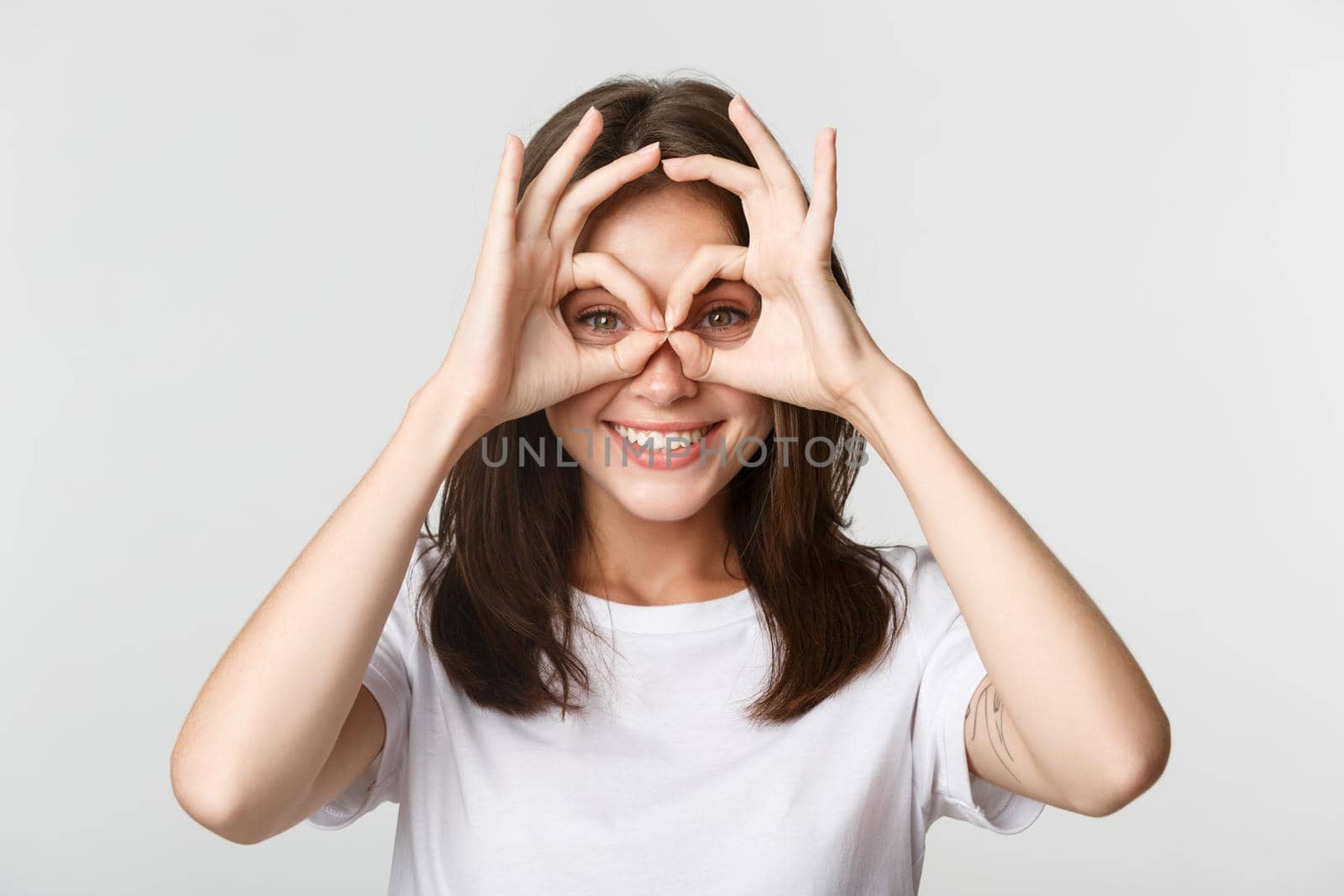 Close-up of happy smiling brunette girl looking through okay gestures, hand glasses, white background.