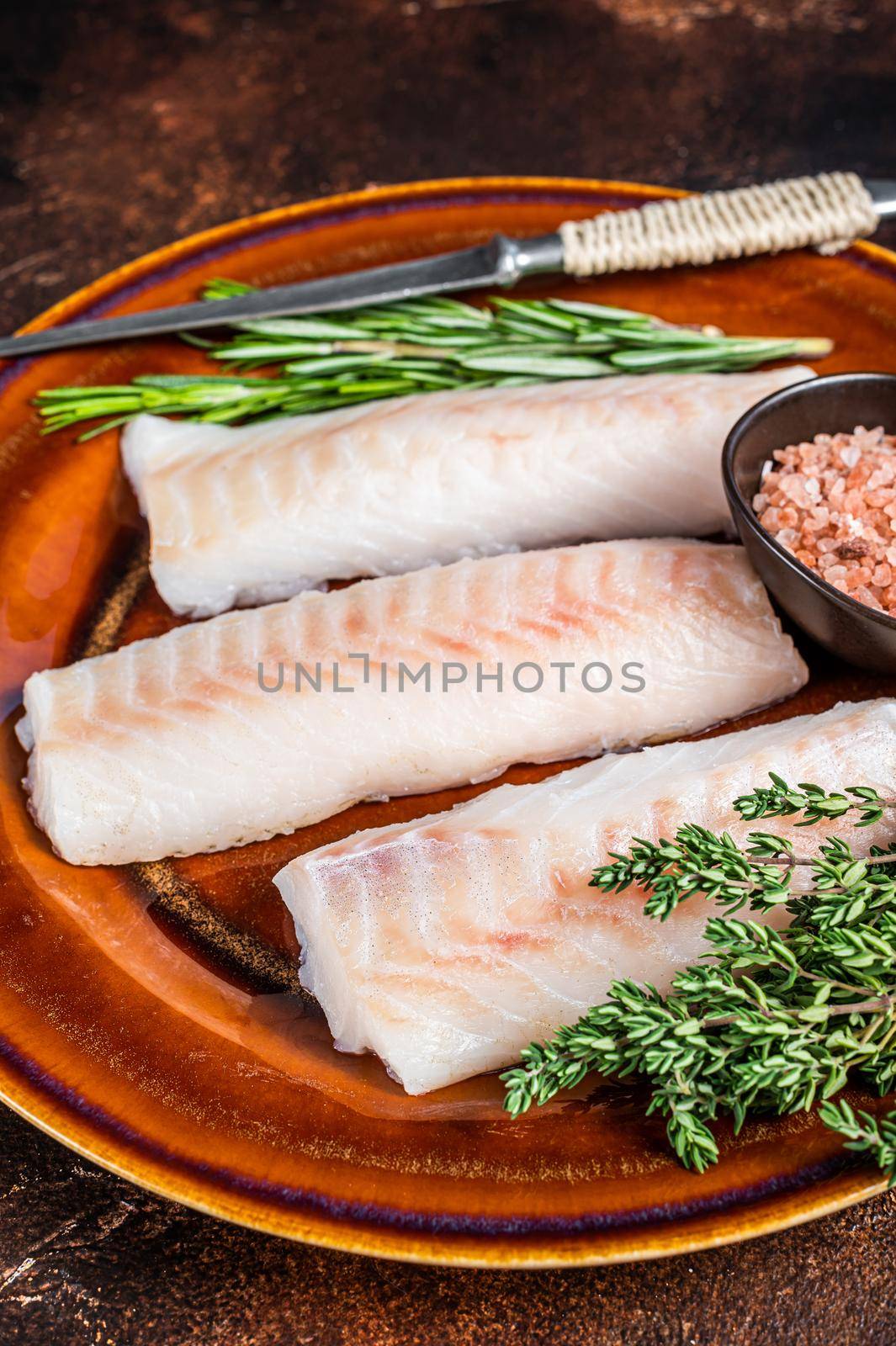 Raw cod loin fillet steaks on rustic plate with thyme and salt. Dark background. Top view.