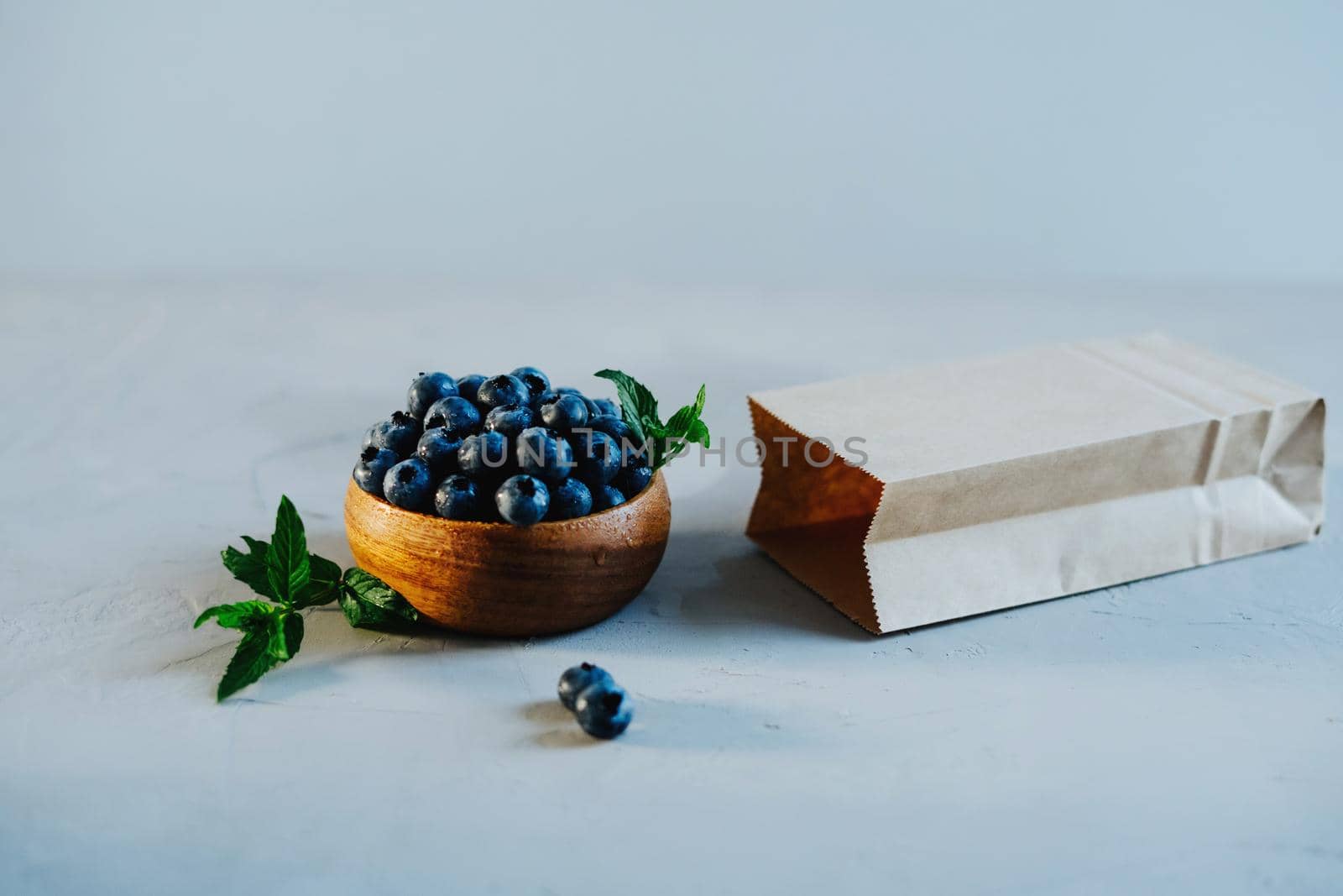 Wooden bowl with fresh blueberries and mint. A kraft bag for berries lies nearby.